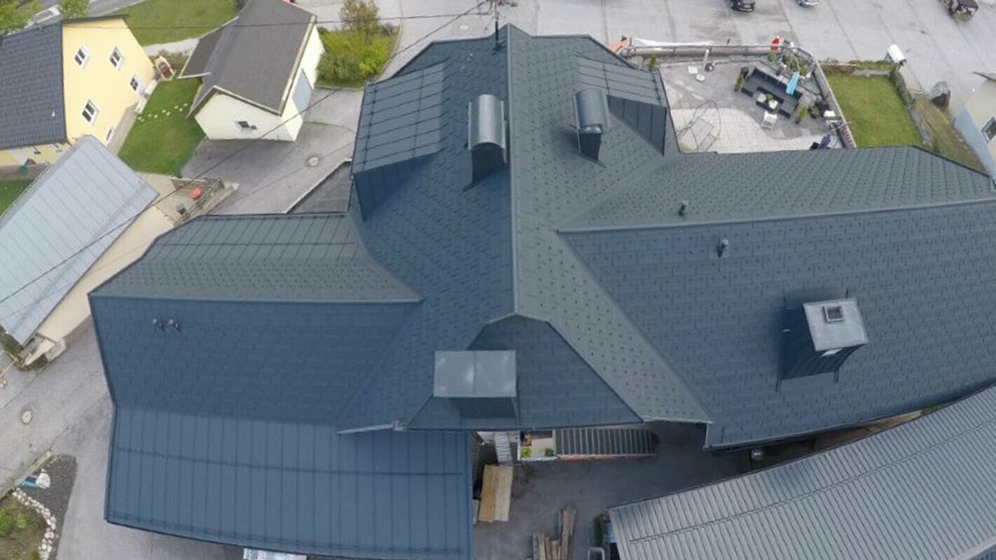 Modernizacja dachu o dużej powierzchni z wieloma szczegółami, koszami dachowymi, oknami dachowymi i kominami. Dach jest kryty aluminiową płytą dachową R.16 firmy PREFA w kolorze antracytowym.