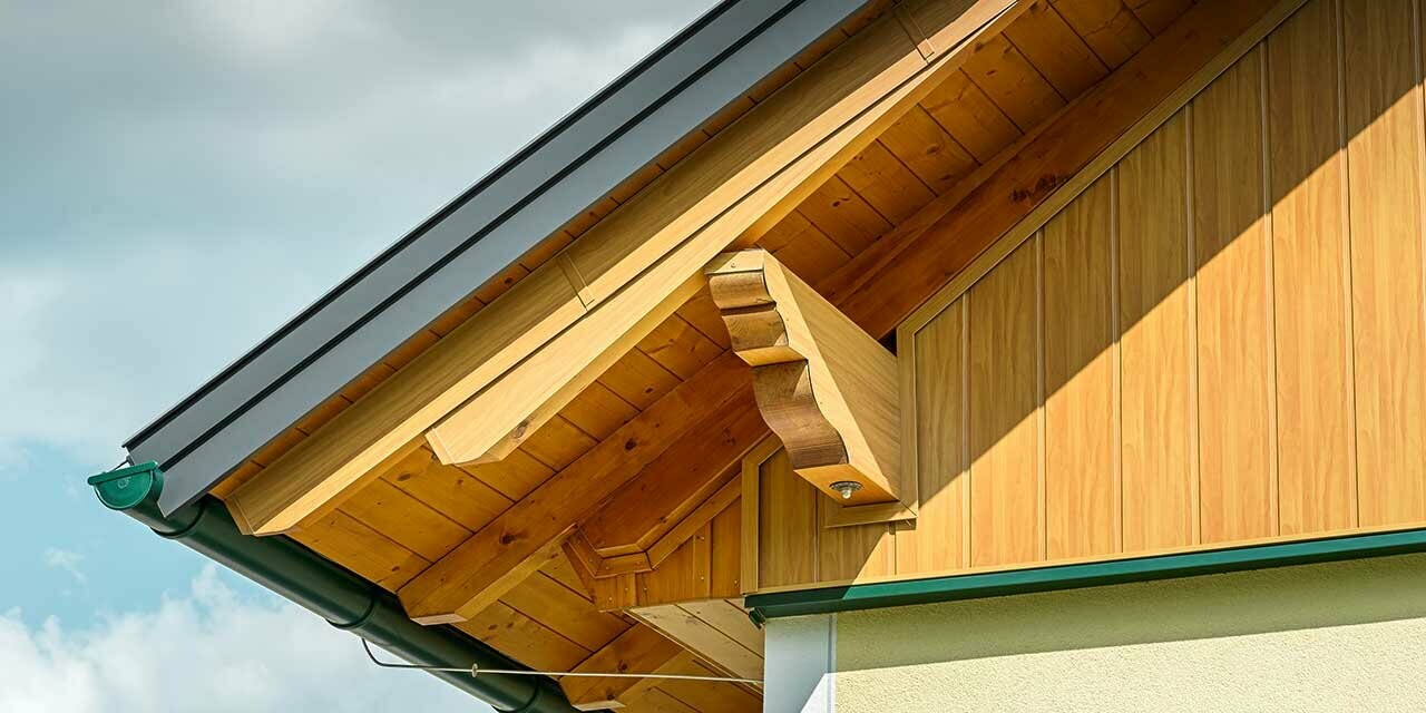 Zbliżenie poszycia ściany szczytowej z sidingiem PREFA o wyglądzie drewna z zieloną rynną dachową.