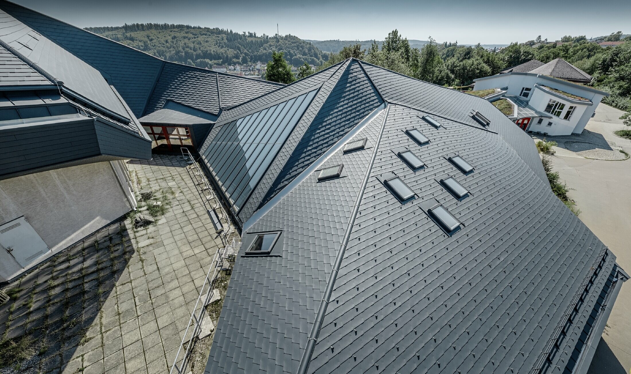 Szkoła „Waldorfschule” w Heidenheim z nowo wyremontowanym dachem: duża powierzchnia dachowa z wieloma załamaniami i pochyłościami została pokryta dachówką łupkową PREFA w kolorze antracytu