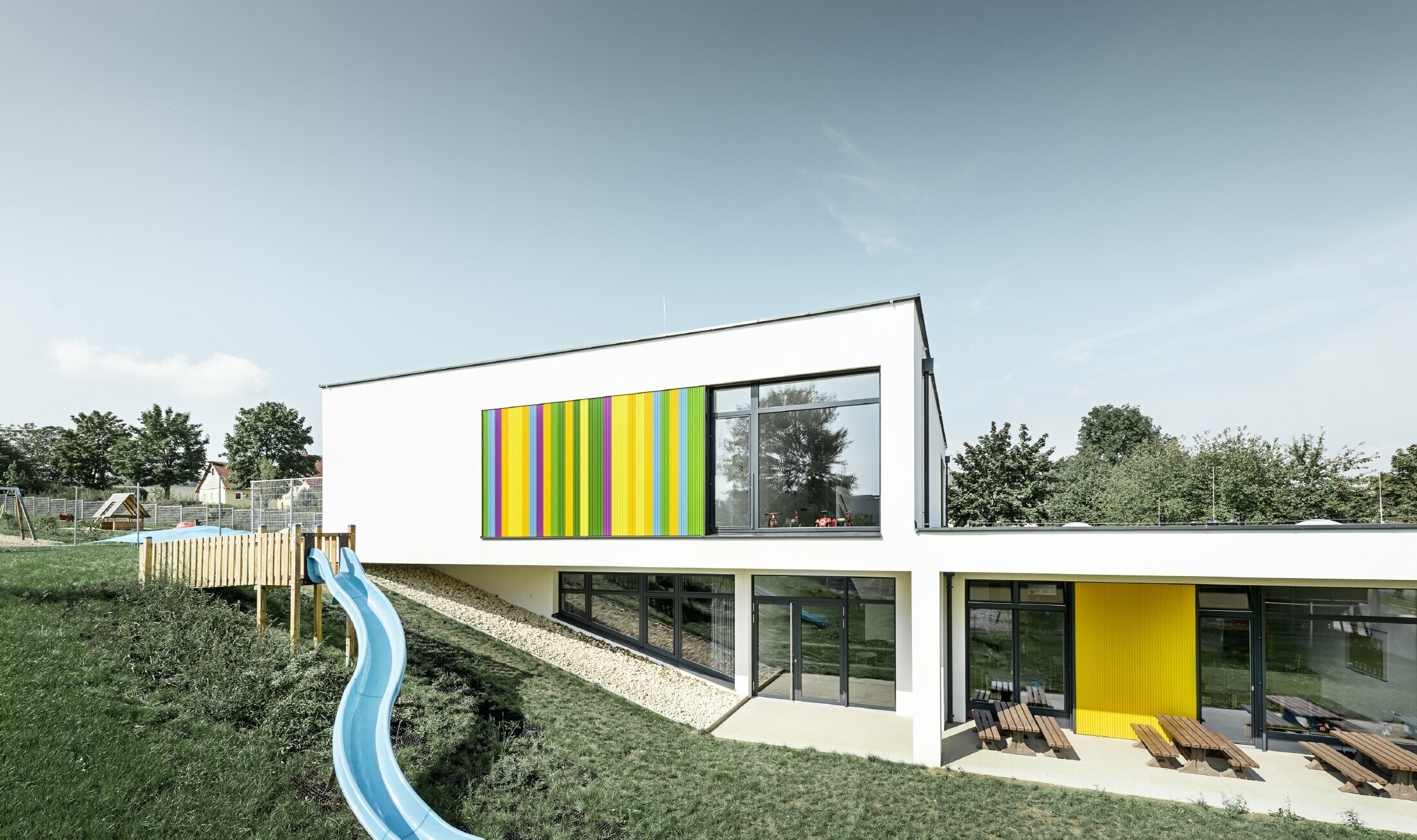 Widok od tyłu przedszkola w Hargelsbergu z kolorowym profil trójkątnym PREFA w kolorach żółtym, zielonym, fioletowym i niebieskim