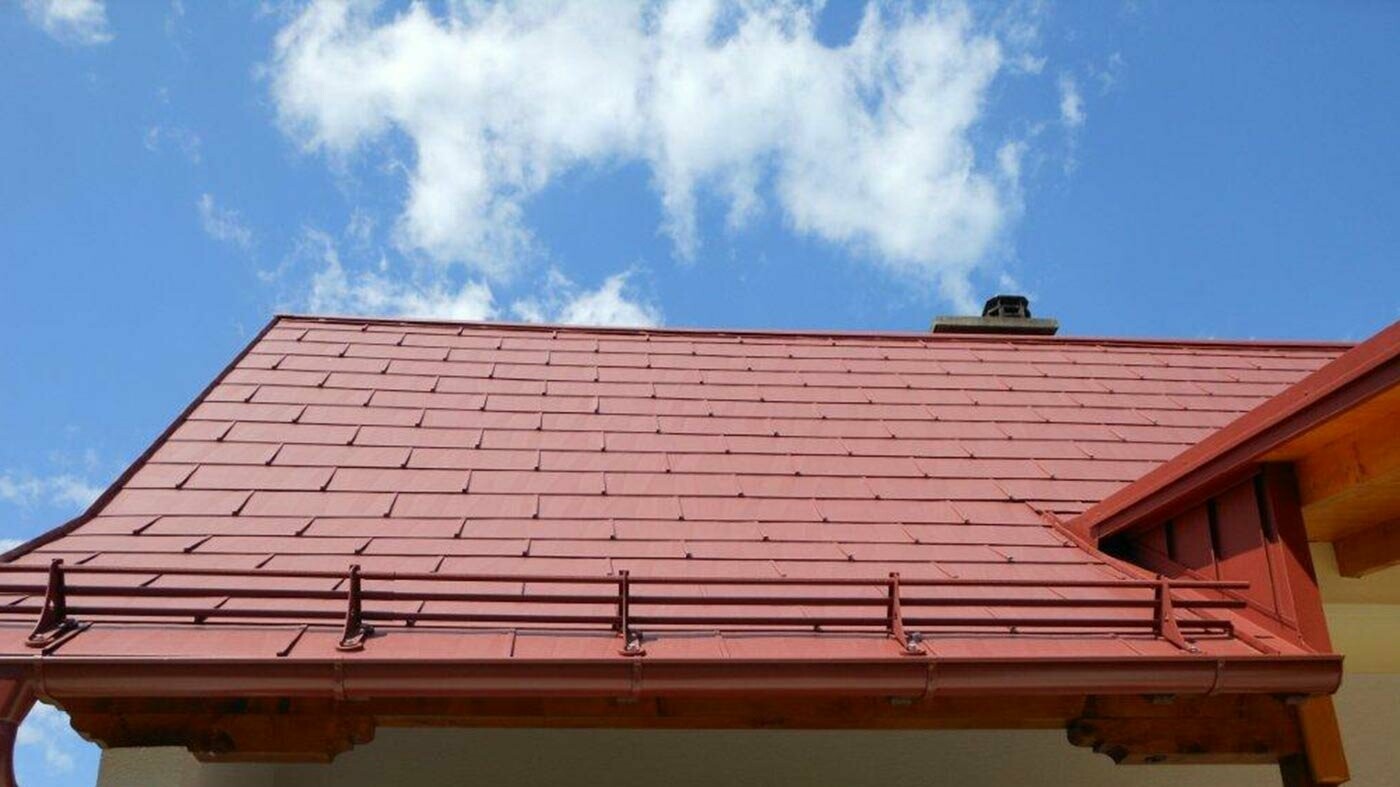 Szczegółowe ujęcie powierzchni dachu z panelem dachowym PREFA FX.12 w kolorze czerwonym tlenkowym z systemem kratek śniegowych.
