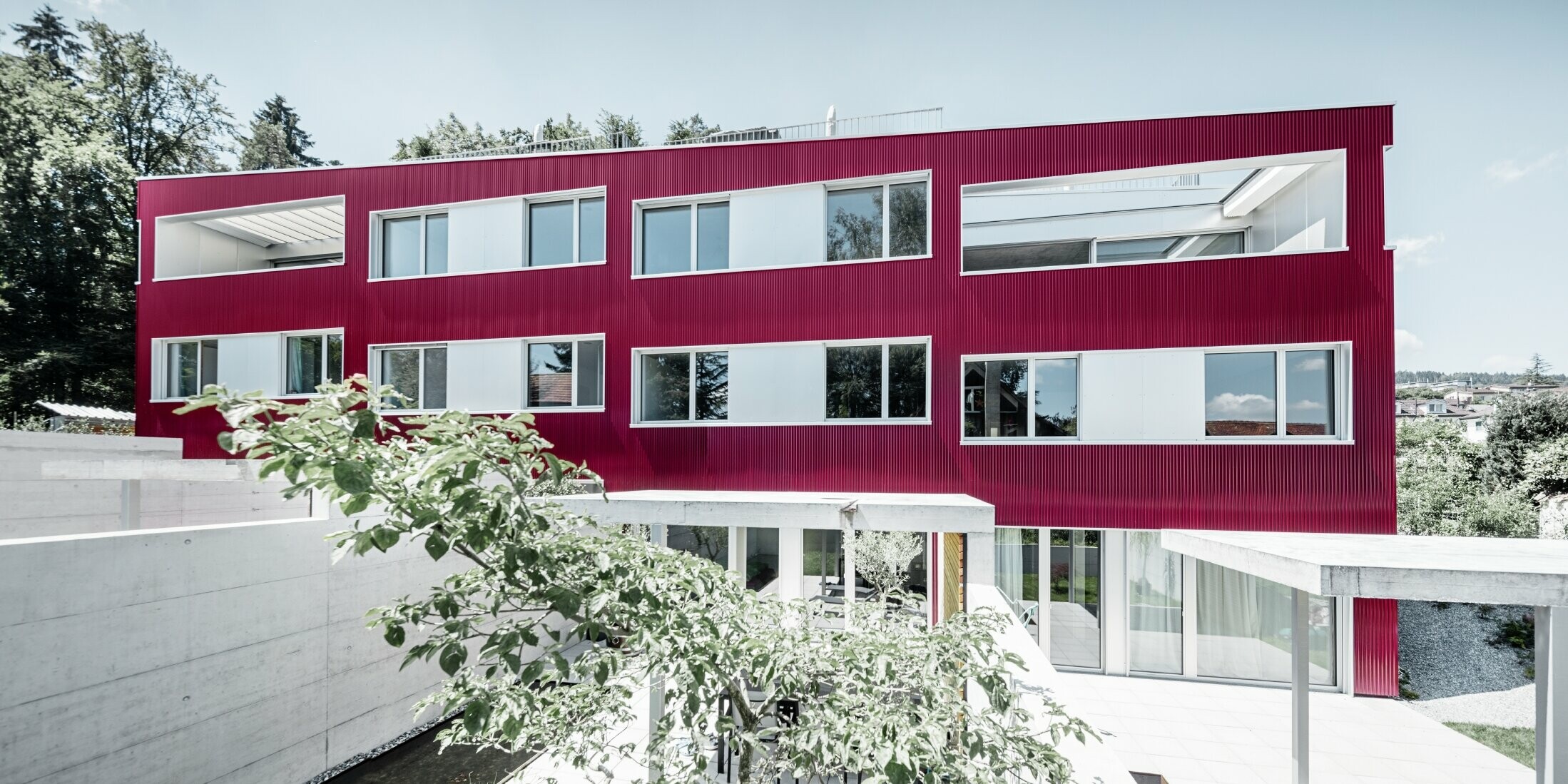 Osiedle mieszkalne z budynkami z płaskimi dachami i balkonami, z elewacją w kolorze czerwonym z profilem falistym PREFA 