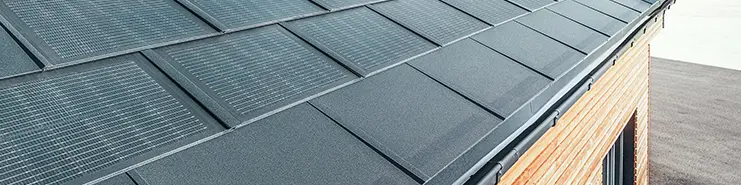 Dachówka solarna PREFA w wersji dużej w połączeniu z dachówką klasyczną R.16 w kolorze czarnym, rynną prostokątną i elewacją z drewna modrzewiowego