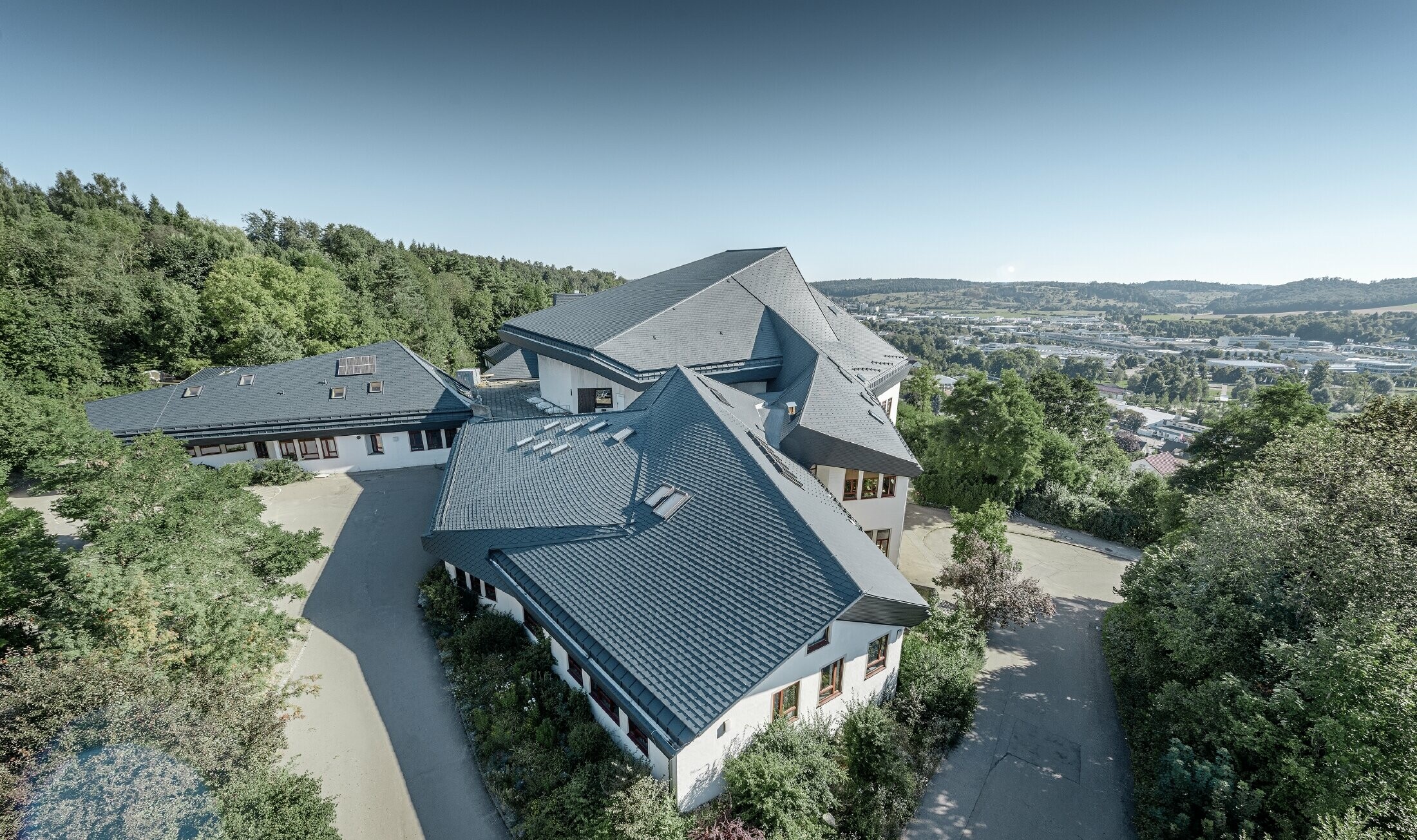 Szkoła „Waldorfschule” w Heidenheim z nowo wyremontowanym dachem: duża powierzchnia dachowa z wieloma załamaniami i pochyłościami została pokryta dachówką łupkową PREFA w kolorze antracytu