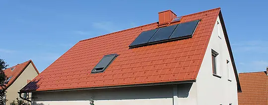 Dom jednorodzinny z dachem dwuspadowym pokryty dachówką klasyczną PREFA w kolorze ceglastym. Powierzchnia dachu wraz z panelami słonecznymi i oknem dachowym