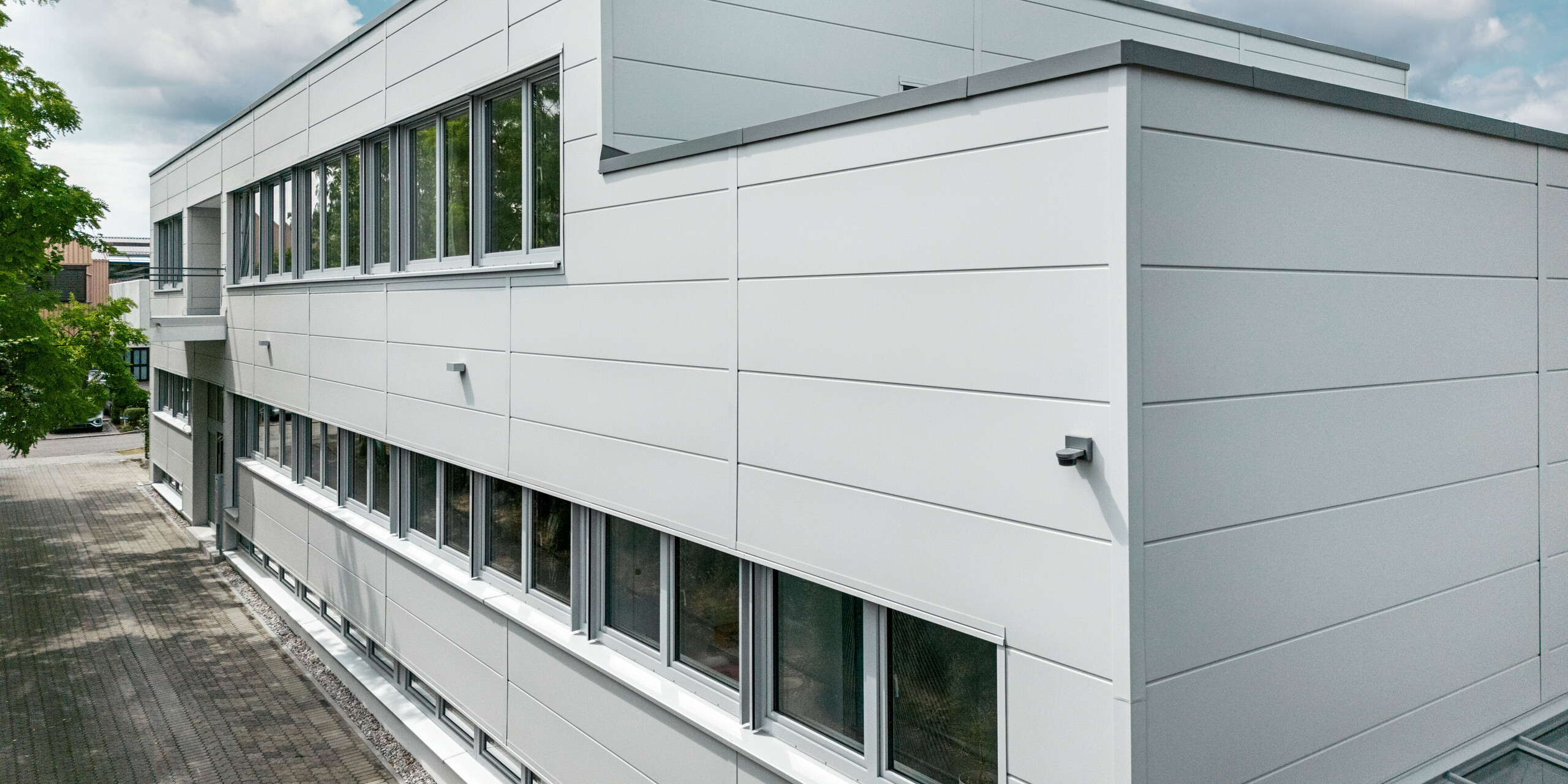 Großformatige PREFA Sidings umhüllen ein Firmengebäude in Oberschleißheim (Deutschland). Die extrabreiten Fassadenelemente aus Aluminium sind in der Farbe Prefaweiß gehalten.