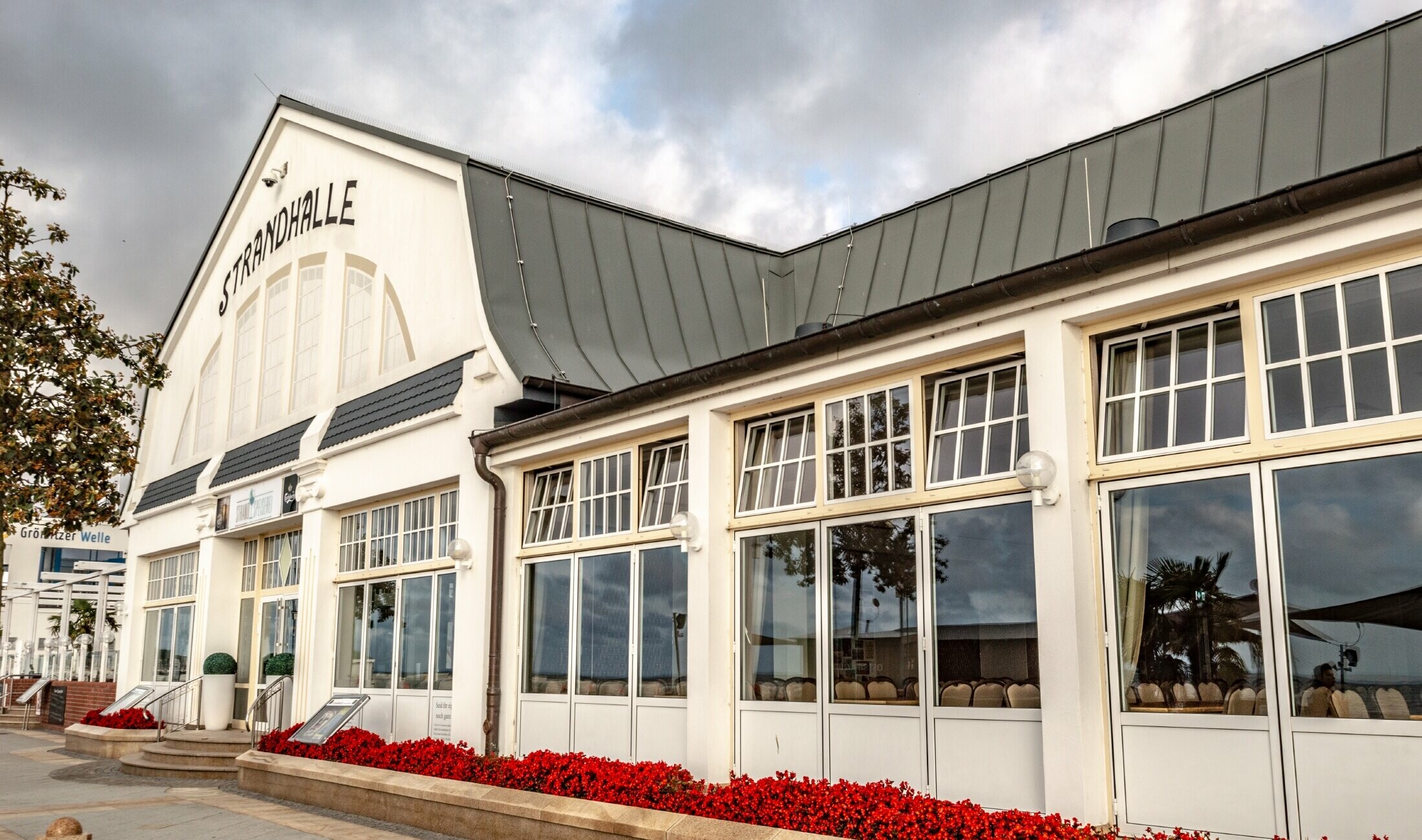 Restauracja Strandhalle w Grömitz z dachem na rąbek stojący PREFA w kolorze jasnoszarym i dużymi oknami do poziomu plaży.