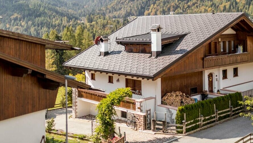 Tradycyjny dom z orzechowobrązowym pokryciem dachowym PREFA i elewacją z elementami drewnianymi i tynkiem