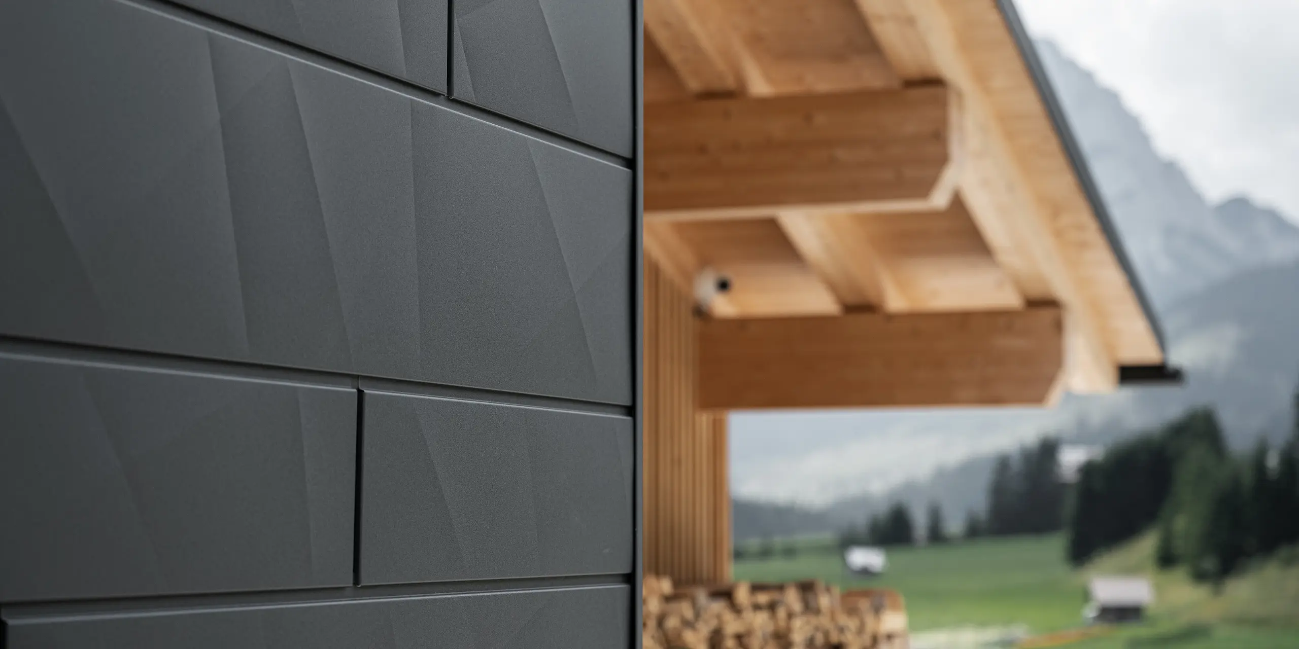 Zbliżenie paneli elewacyjnych Siding.X w kolorze P.10 czarny od PREFA na budynku Casa Hoffe w Sappadzie we Włoszech. Aluminiowy system elewacyjny został umiejętnie zastosowany w nowoczesnym, abstrakcyjnym układzie, który tworzy atrakcyjny kontrast z widocznymi drewnianymi elementami więźby dachowej. Innowacyjne rozwiązanie elewacyjne harmonijnie wpisuje się w alpejskie otoczenie i symbolizuje połączenie funkcjonalności, trwałości oraz estetycznej kultury budowlanej.