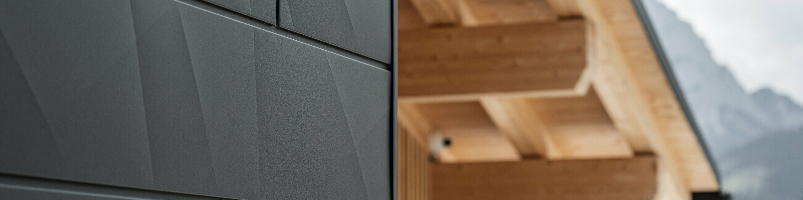 Zbliżenie paneli elewacyjnych Siding.X w kolorze P.10 czarnym firmy PREFA na budynku Casa Hoffe w Sappadzie we Włoszech. System elewacyjny z aluminium został umiejętnie zastosowany w nowoczesnym, abstrakcyjnym projekcie, który stanowi atrakcyjny kontrast dla widocznych elementów drewnianych konstrukcji dachu. Innowacyjne rozwiązanie elewacyjne idealnie komponuje się z alpejskim otoczeniem i stanowi połączenie funkcjonalności, trwałości i estetycznej kultury budowlanej.