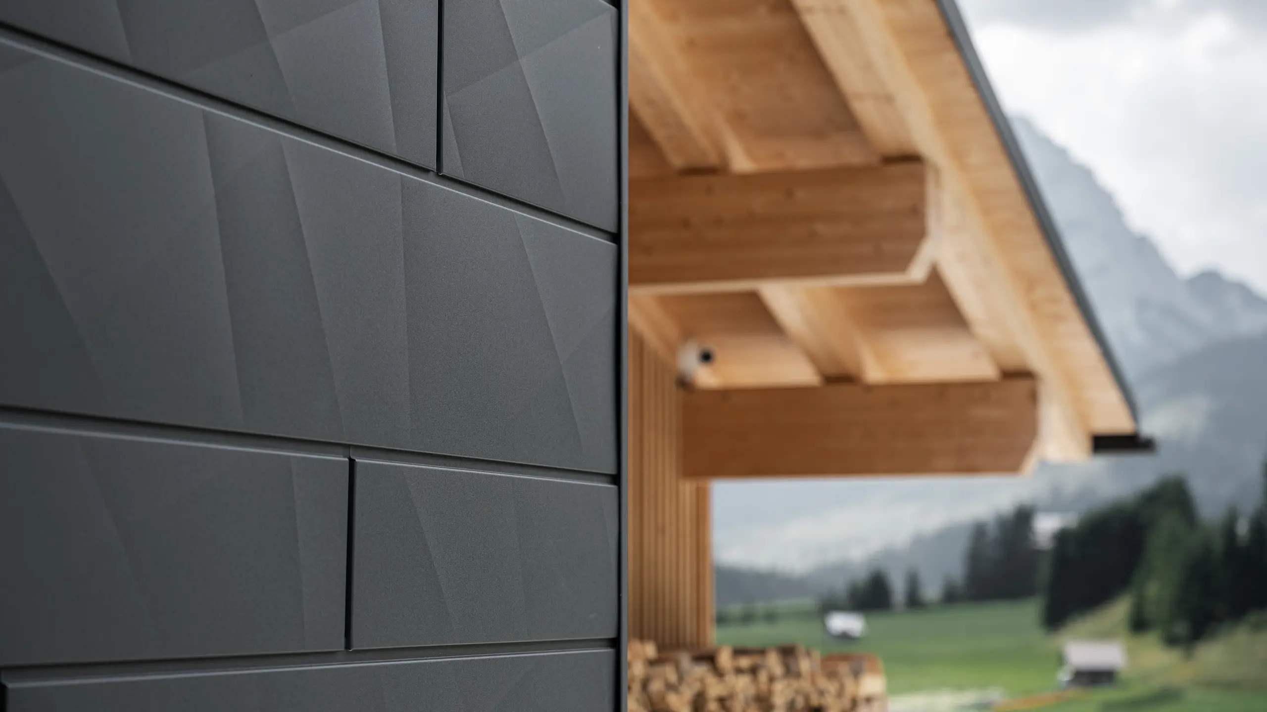 Zbliżenie paneli elewacyjnych Siding.X w kolorze P.10 czarny od PREFA na budynku Casa Hoffe w Sappadzie we Włoszech. Aluminiowy system elewacyjny został umiejętnie zastosowany w nowoczesnym, abstrakcyjnym układzie, który tworzy atrakcyjny kontrast z widocznymi drewnianymi elementami więźby dachowej. Innowacyjne rozwiązanie elewacyjne harmonijnie wpisuje się w alpejskie otoczenie i symbolizuje połączenie funkcjonalności, trwałości oraz estetycznej kultury budowlanej.