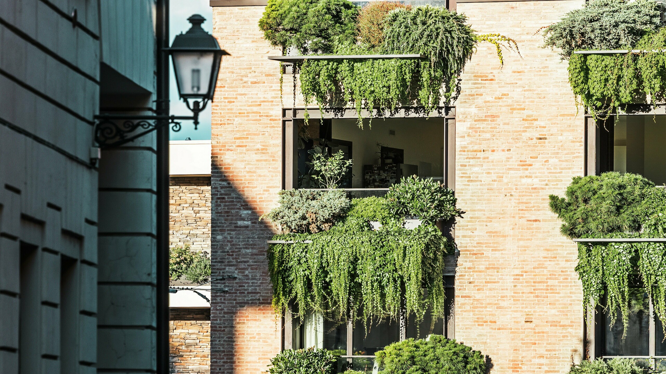 Szczegółowy widok zielonej fasady z cegły we Włoszech z wiszącymi ogrodami, detalami architektonicznymi PREFALZ i przylegającą starówką z latarnią.