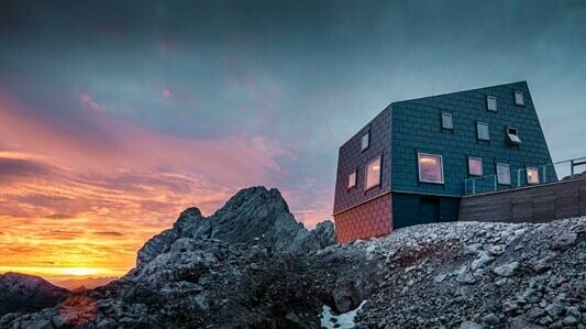 Niezwykła architektura w górach: schronisko Seethalerhütte na Dachstein pokryte panelami dachowymi oraz elewacyjnymi PREFA Fx.12 w kolorze szarym kamiennym.
