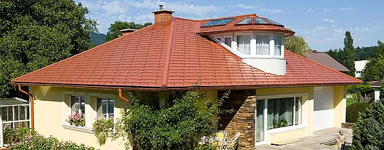 Bungalow z żółtą elewacją i dachem PREFA pokrytym czerwoną dachówką.