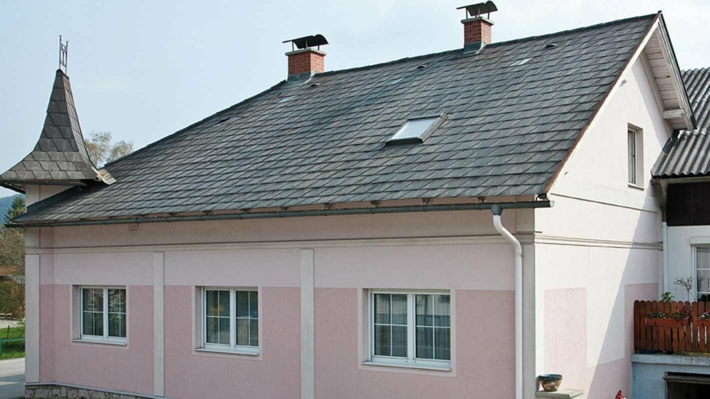 Dom przed modernizacją dachu z płytą dachową PREFA w Austrii — wcześniej cement włóknisty, eternit, z wieżyczkami, czerwona elewacja