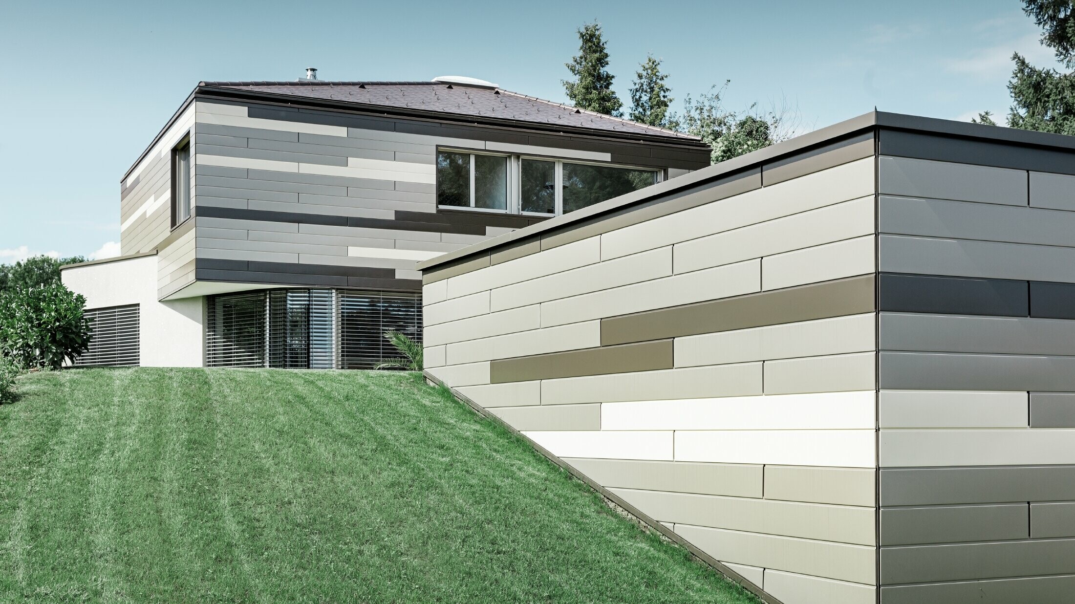 Nowoczesny dom jednorodzinny z płaskim dachem i zadaszonym tarasem, z indywidualnie zaprojektowaną elewacją aluminiową wykonaną z sidingu PREFA w kolorze brązowym, brązu i kości słoniowej