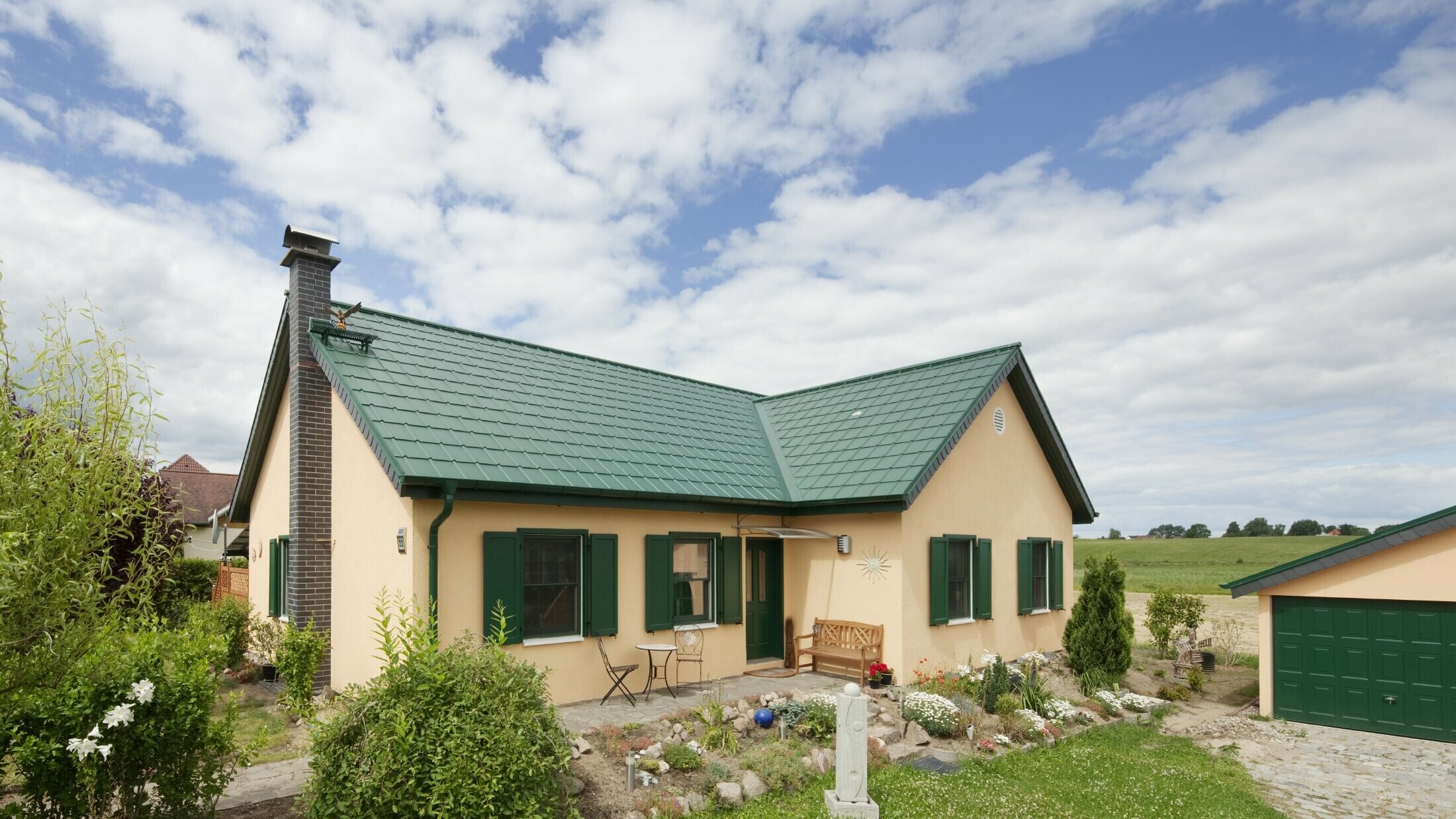 erweitertes Satteldach; Satteldach in L-Form; mit der PREFA Dachplatte in P.10 Moosgrün; hübsches ländliches Häuschen mit zum PREFA Dach passenden grünen Fensterläden.