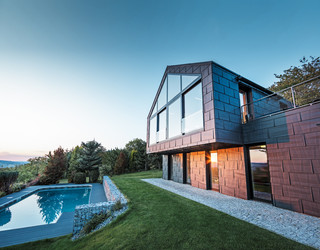 Elewacja aluminiowa domu jednorodzinnego z panelami elewacyjnymi PREFA FX.12 w kolorze antracyt P.10 przy zachodzie słońca. 