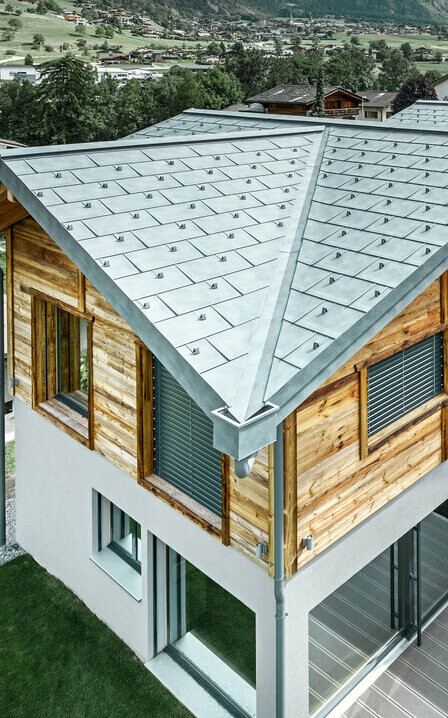 Szwajcarski dom letniskowy z aluminiowym dachem PREFA. Wykorzystana została dachówka klasyczna R.16 PREFA w kolorze szarym kamiennym. Na górnym piętrze wykonano rustykalną elewacją drewnianą.