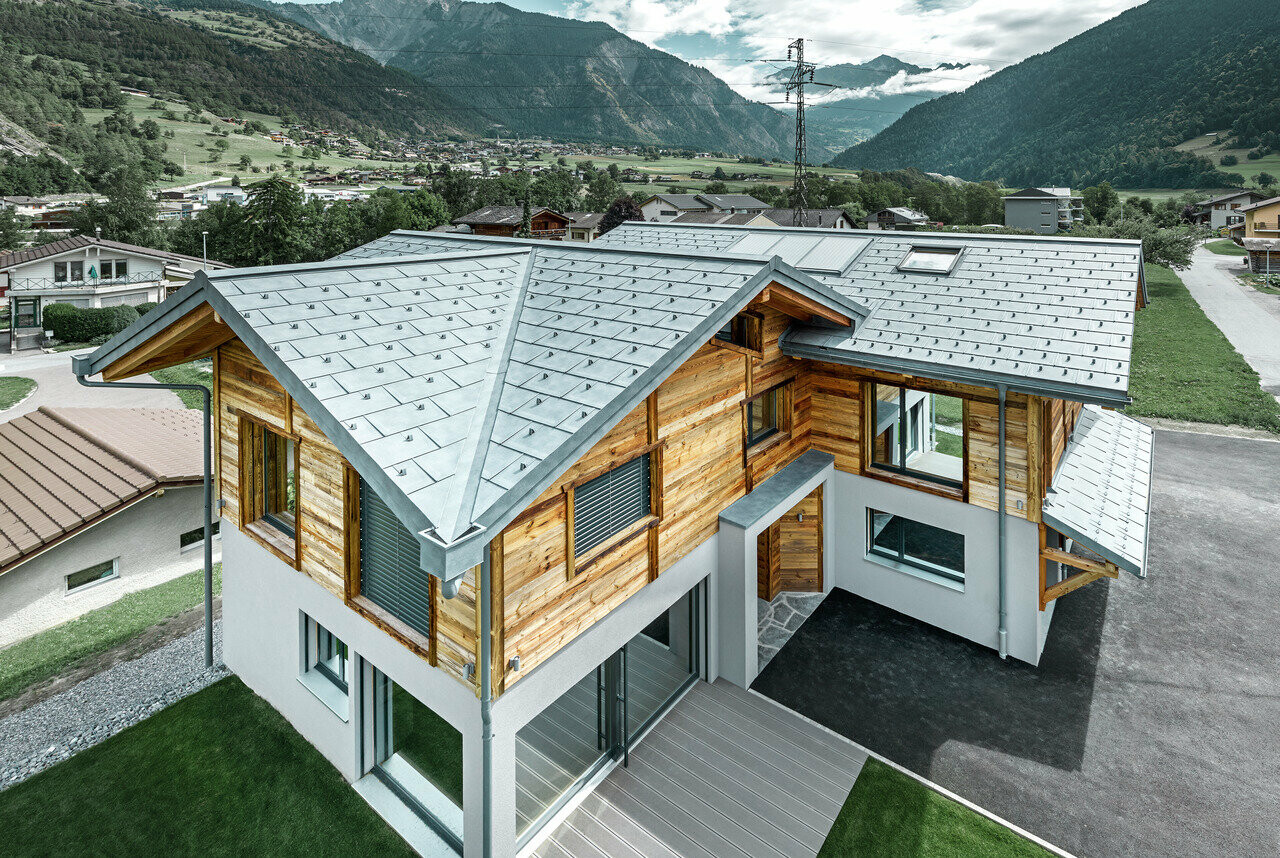 Szwajcarski dom letniskowy z aluminiowym dachem PREFA. Wykorzystana została dachówka klasyczna R.16 PREFA w kolorze szarym kamiennym. Na górnym piętrze wykonano rustykalną elewacją drewnianą.