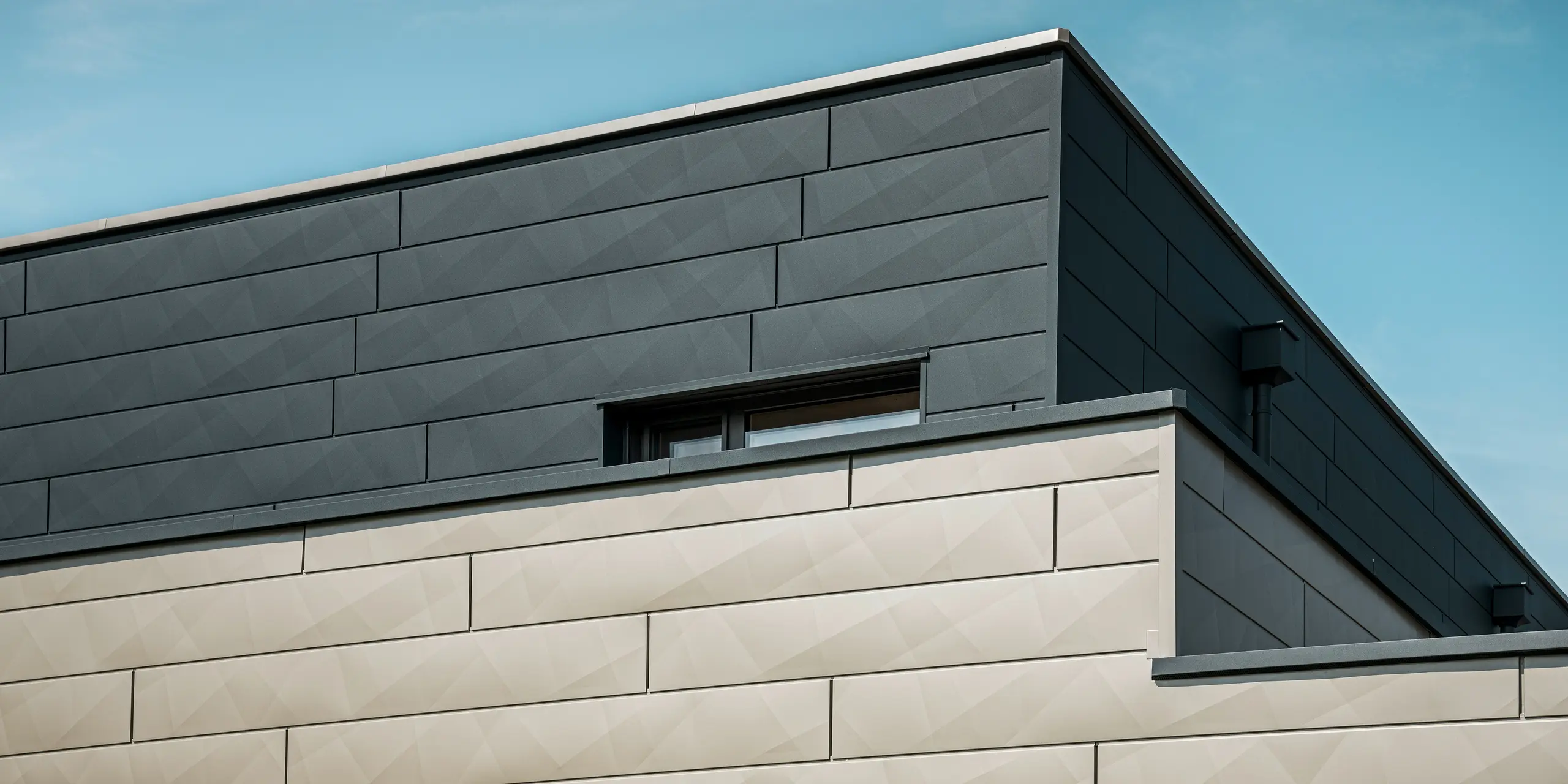 [Translate to Polski:] Nahaufnahme der zweifarbigen PREFA Aluminiumfassade eines modernen Einfamilienhauses in Wippenham, Österreich. Die Fassade ist mit Siding.X Fassadenpaneelen in den Farben Anthrazit und Bronze gestaltet, die ein elegantes und dynamisches Erscheinungsbild erzeugen. Die präzise Verarbeitung und das Zusammenspiel der Farben betonen die zeitgemäße Architektur des Gebäudes.