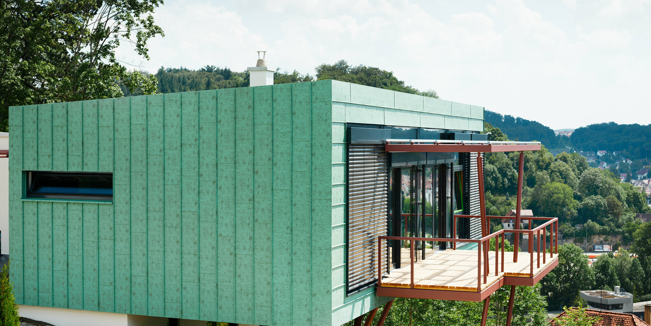 Das Heidenheimer Wohnhauses wird umhüllt von einer markanten PREFALZ-Fassade in Patina-Grün, die in der Sonne glänzt. Die perfekte Kombination aus Funktionalität und Design wird durch die widerstandsfähigen Eigenschaften der PREFALZ-Fassade verstärkt. Sie trotzt nicht nur dem Wetter, sondern garantiert auch eine lange Lebensdauer. Diese Fassade hebt die Schönheit und Beständigkeit des Gebäudes auf ein neues Niveau.