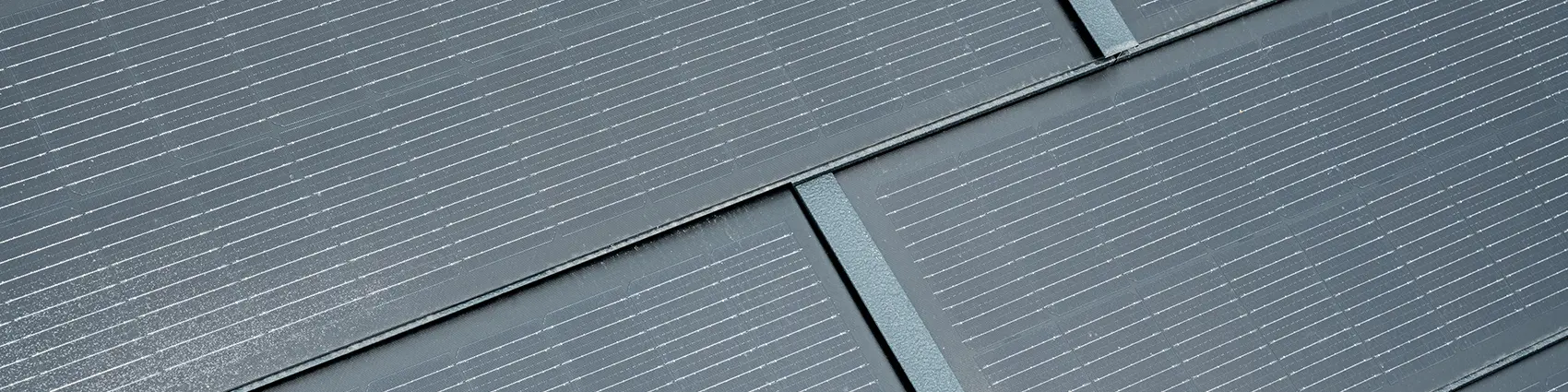 Szczegółowe zdjęcie ułożonej małej dachówki solarnej. Mała dachówka solarna w kolorze P.10 antracytowym została połączona z dachówką klasyczną R.16. 