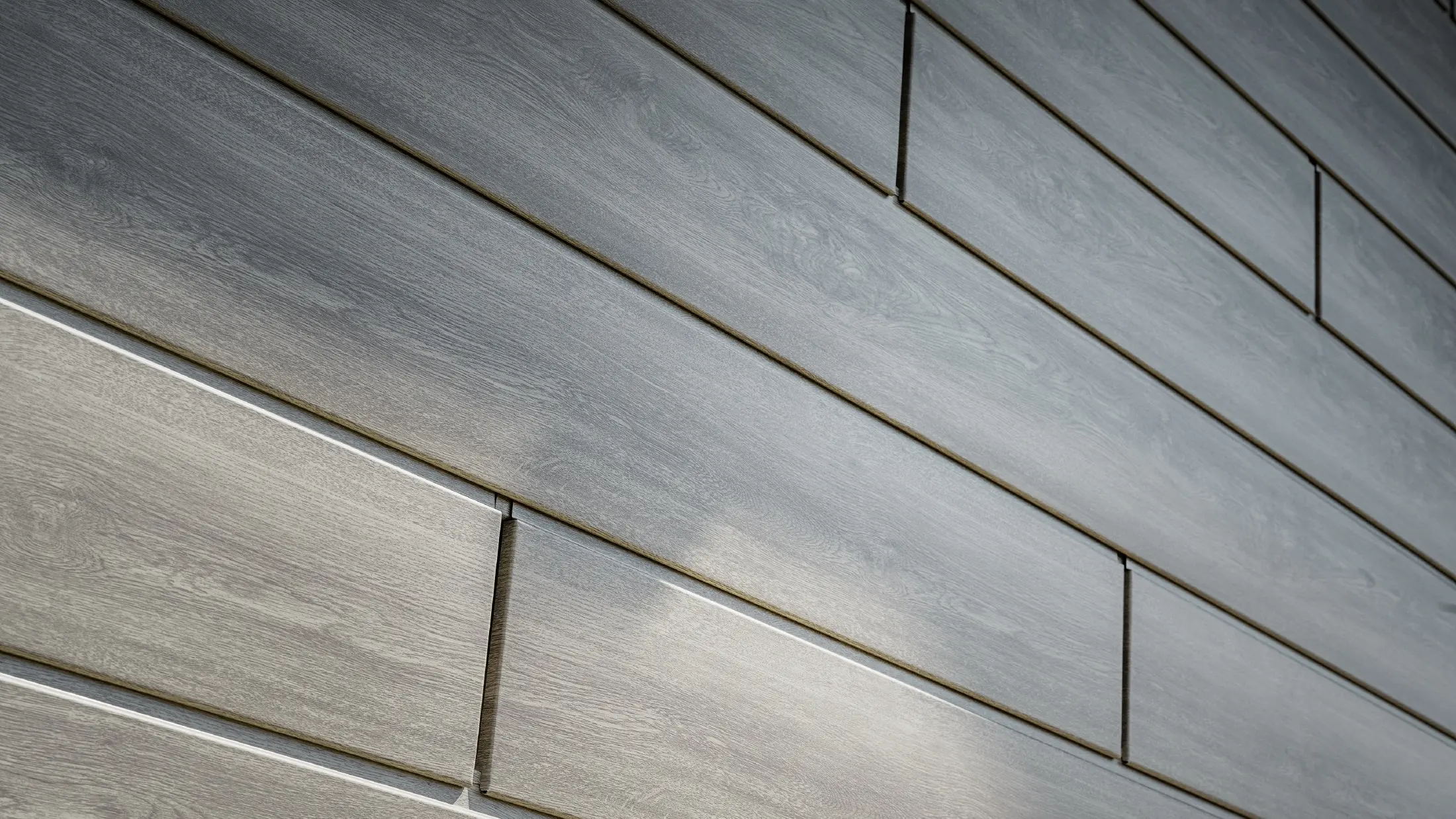 Zbliżenie na elewację aluminiową PREFA Siding. Panele aluminiowe zostały ułożone poziomo i mają wygląd drewna – dąb szary.