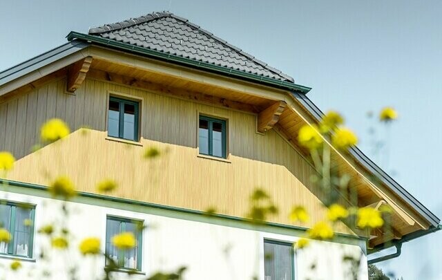 Ściany szczytowe obkładane panelami aluminiowymi PREFA w kolorze drewna (dąb naturalny), siding układany pionowo włącznie z podbitką dachu