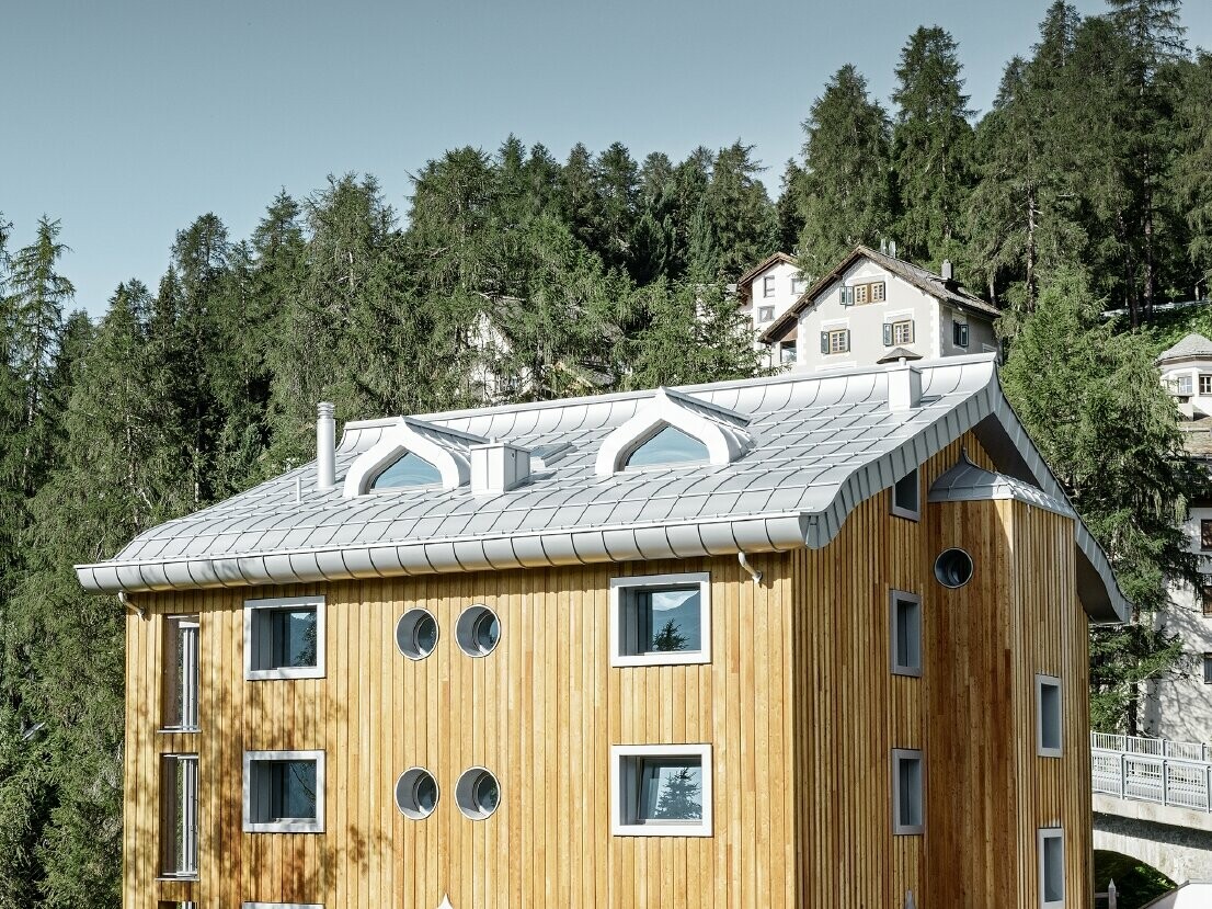 Osiedle mieszkaniowe w St. Moritz z drewnianą elewacją i dachem aluminiowym z łukowatym okapem w kolorze srebrny metallic