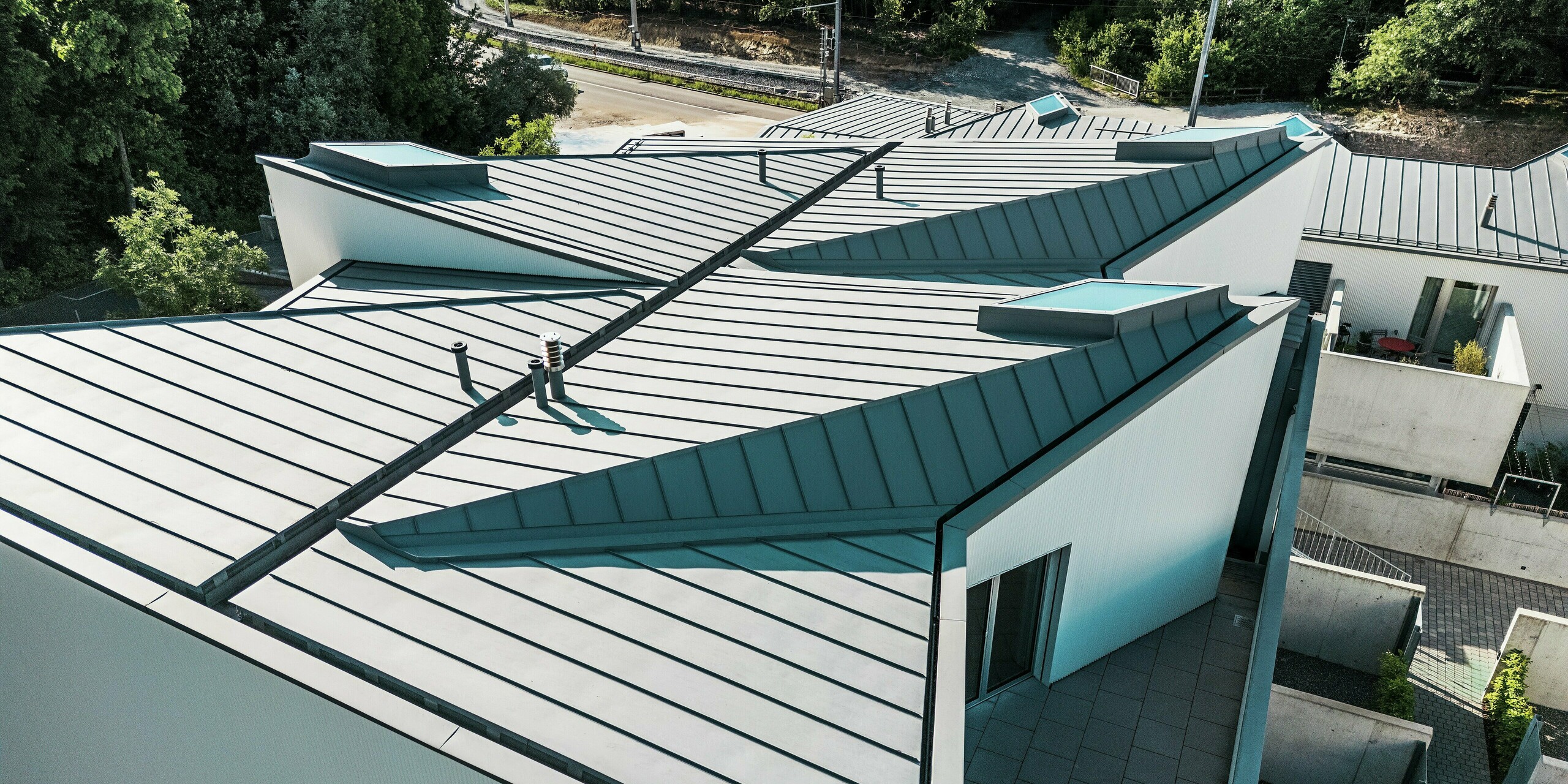 Spektakuläre Dachgeometrie mit PREFALZ in Patinagrau: Die gefalteten Stehfalzdächer der Tiny Homes in Zollikerberg setzen architektonische Akzente und schaffen klare Linien. Die hochwertige PREFA Dachlösung überzeugt durch Langlebigkeit, Wartungsfreiheit und Gestaltungsfreiheit – ideal für komplexe Formen in anspruchsvoller Umgebung wie hier am Hang mit Bahnanschluss.