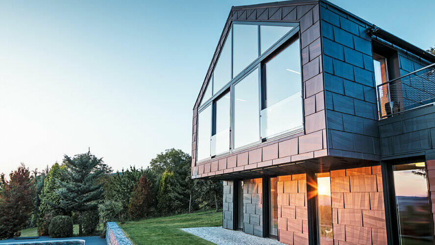 Nowoczesny dom jednorodzinny bez okapu dachowego z dużymi powierzchniami okien i fasadą FX.12 w kolorze antracytowym, sfotografowany o zachodzie słońca.