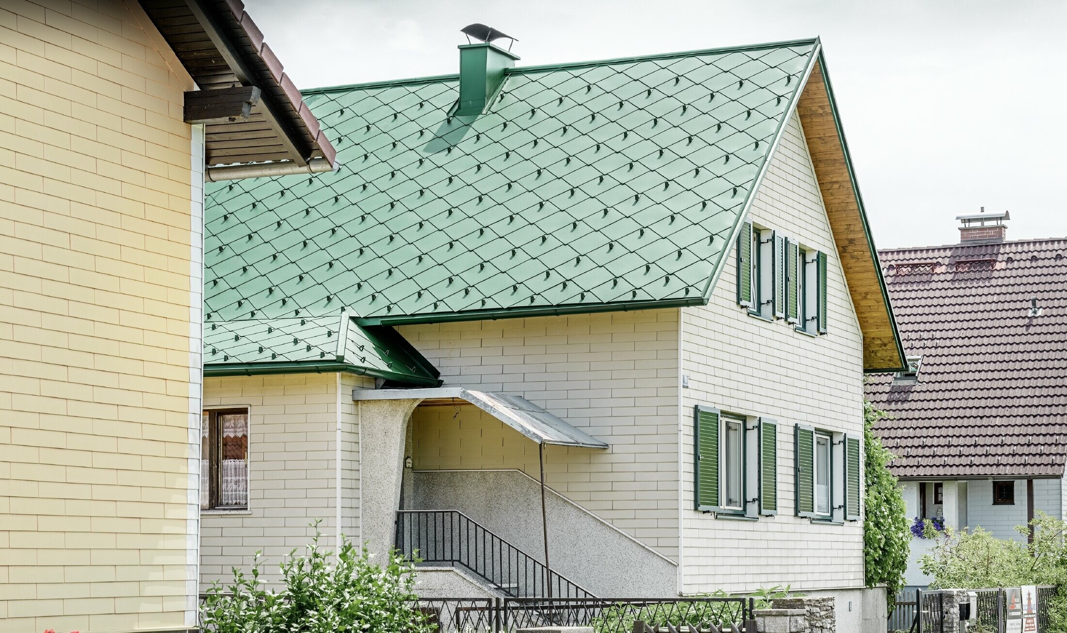 Klasyczny dom jednorodzinny z dachem dwuspadowym z pokryciem dachowym z aluminium w kolorze zieleni mchu i zielonymi okiennicami