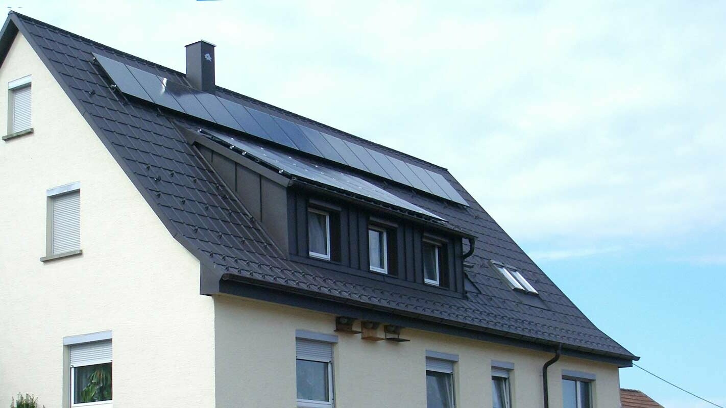 Zmodernizowany dach z płytą dachową PREFA w kolorze antracytu, okno dachowe obłożone blachą Prefalz; na dachu znajduje się instalacja fotowoltaiczna.