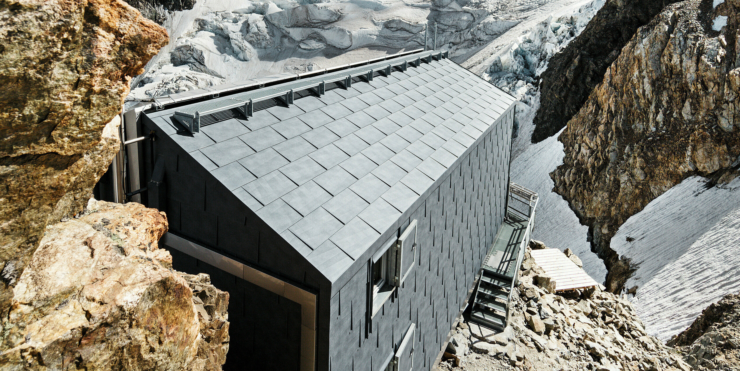 Detailansicht der PREFA Dachpaneele FX.12 des Refuge de l'Aigle in den französischen Alpen, mit Blick auf den umliegenden Gletscher. Die robusten Aluminiumpaneele sind in der Farbe P.10 steingrau ausgeführt und fügen sich harmonisch in die alpine Umgebung ein.