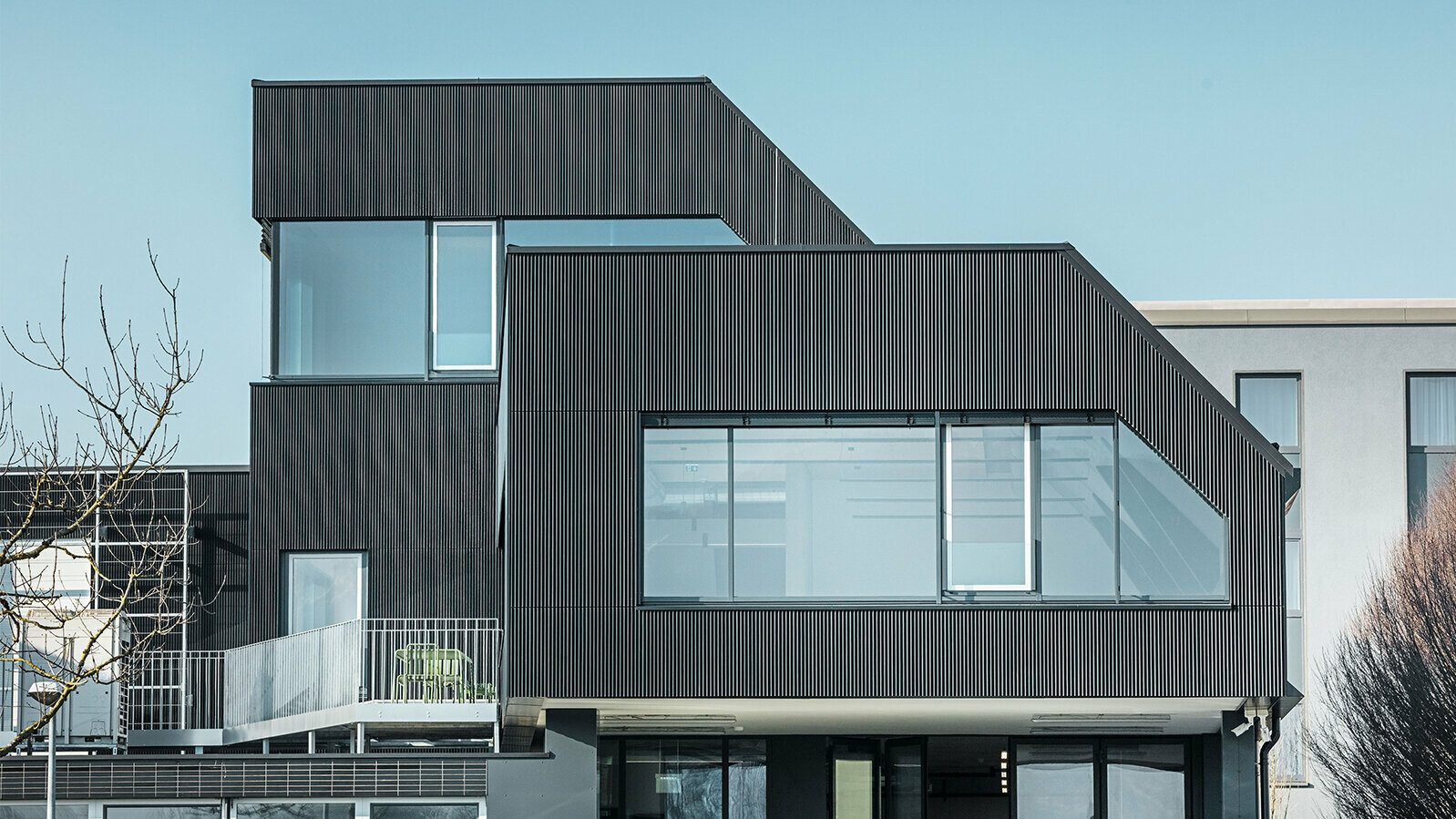 Widok z boku budynku kawiarni Amann w słoneczny dzień. Dla ochrony budynku zastosowano profil falisty w kolorze czarnym.