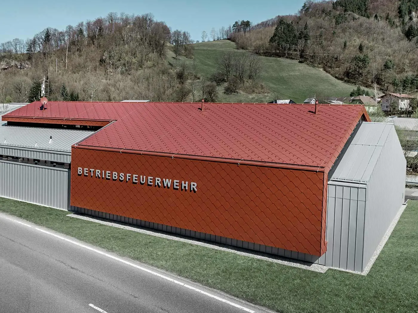 Nowy budynek zakładowej straży pożarnej firm PREFA i Neuman Aluminium został obłożony nowymi dachówkami rombowymi i rombowymi płytami ściennymi 44 x 44 w kolorze P.10 czerwony tlenkowy i blachą Prefalz w kolorze srebrny metallic.