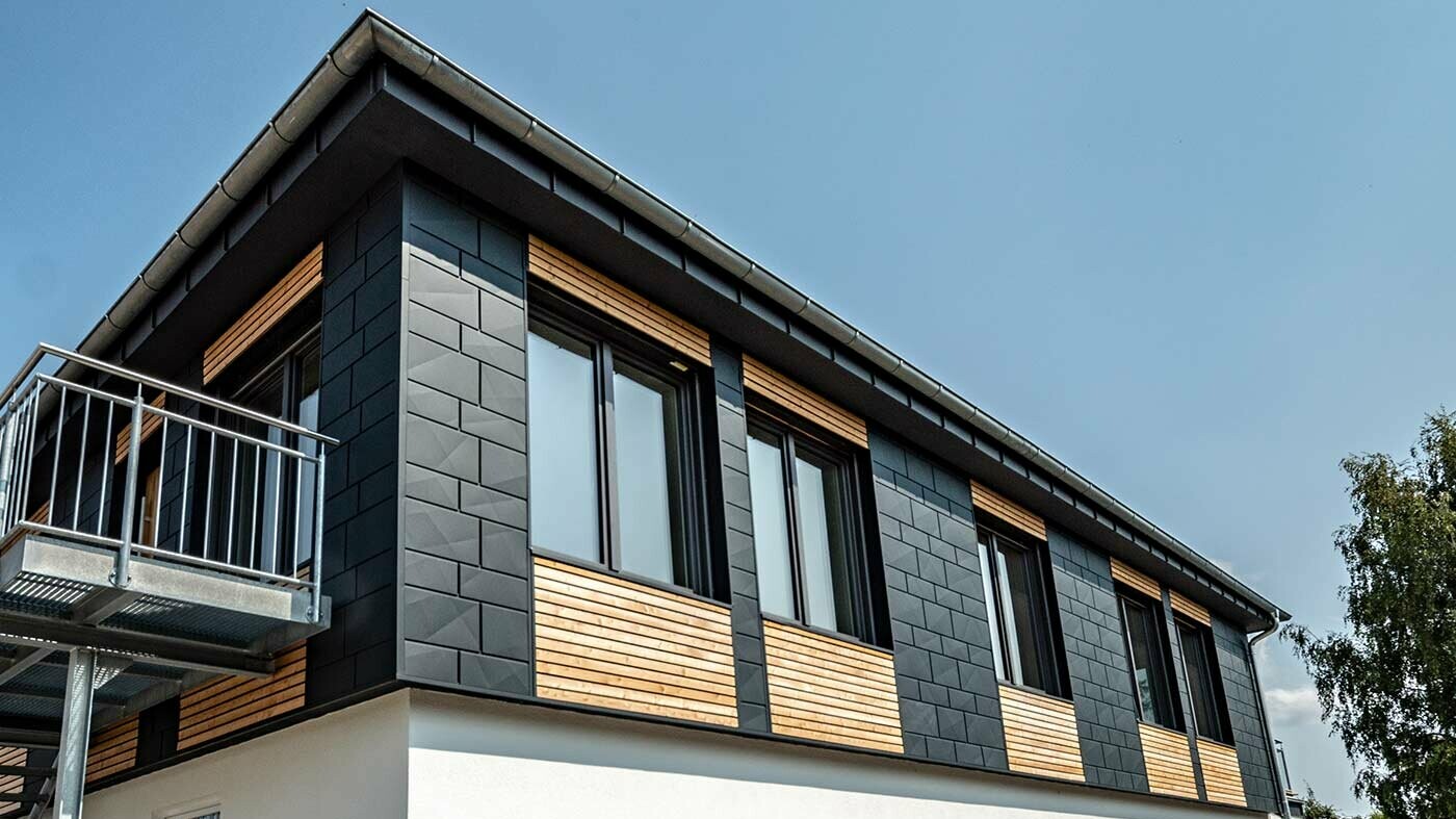 Górna część budynku została obłożona połączeniem poziomych paneli z drewna modrzewiowego i paneli PREFA Siding.X z aluminium w kolorze antracytowym.