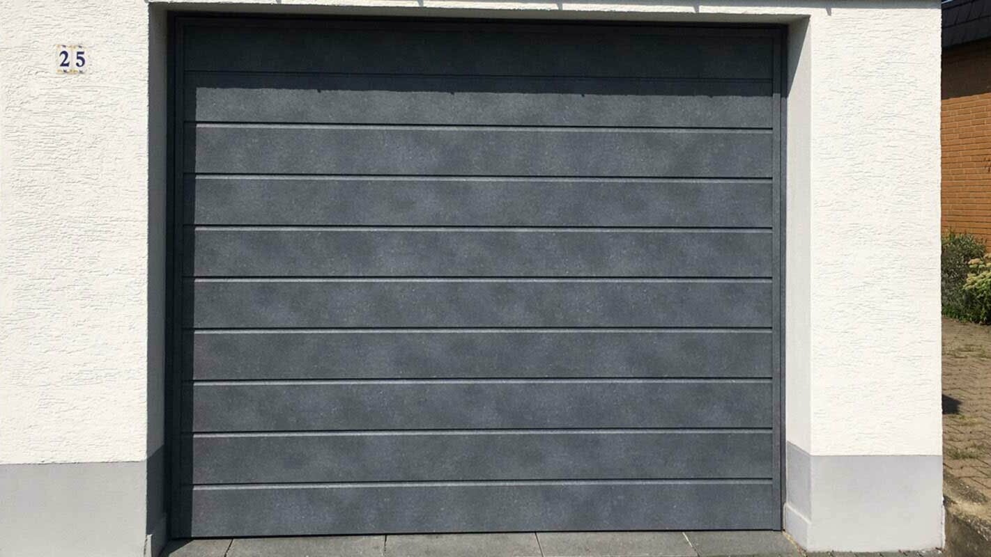Brama garażowa obłożona ułożonymi poziomo sidingami PREFA w kolorze szarym kamiennym