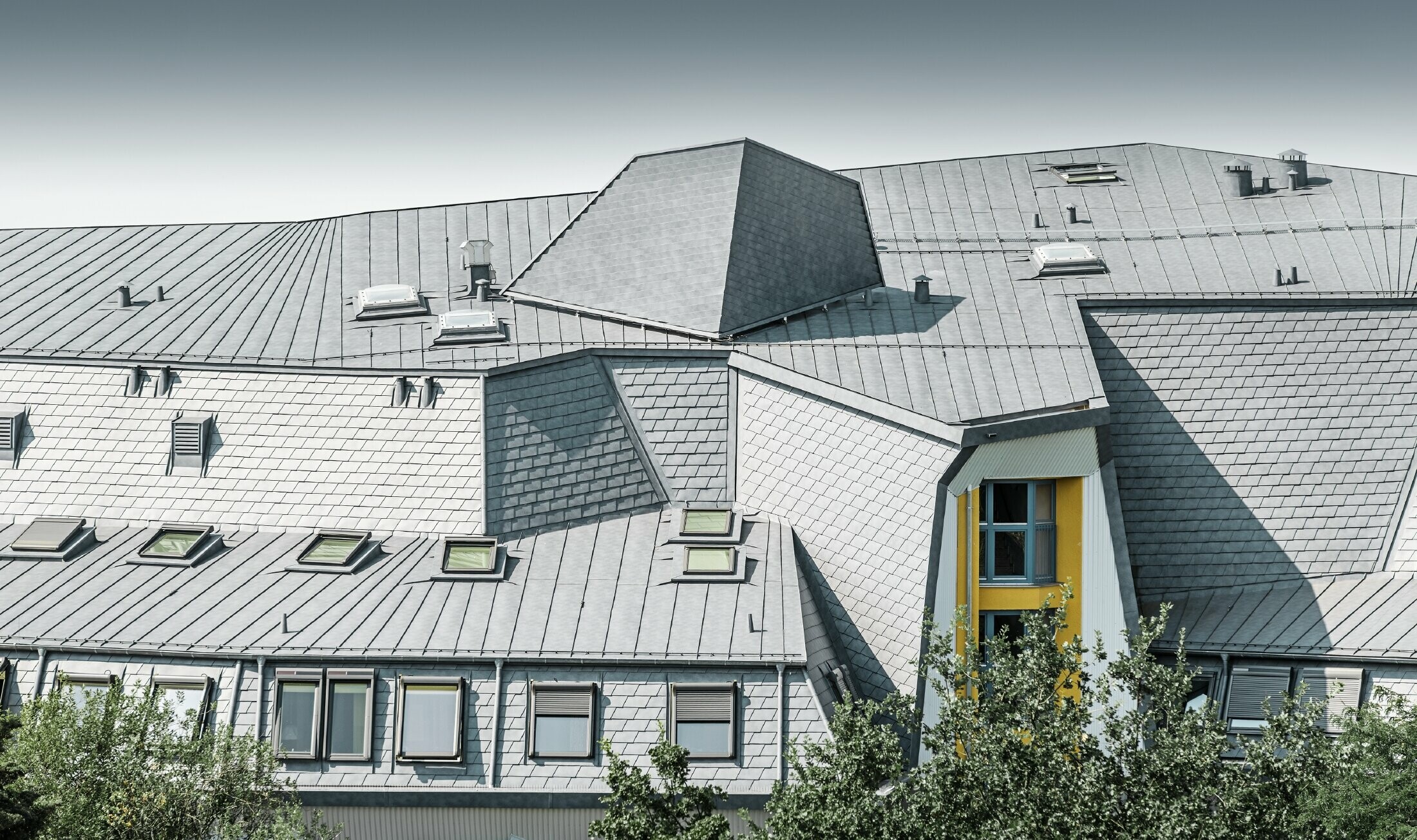 Dach o skomplikowanej sylwetce z lukarnami i zakrzywieniami na Haus Aja Textor-Goethe, pokryty dachówką łupkową i systemem Prefalz PREFA w kolorze szarym kamiennym