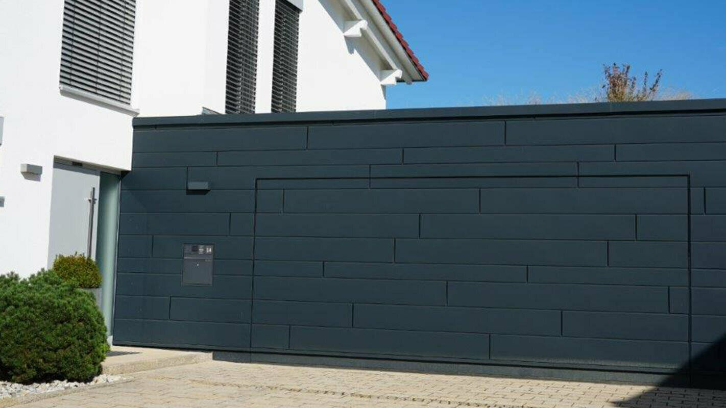 Elewacja garażu po modernizacji z sidingami PREFA w kolorze antracytowym, brama garażowa jest zamontowana w jednej płaszczyźnie z elewacją 