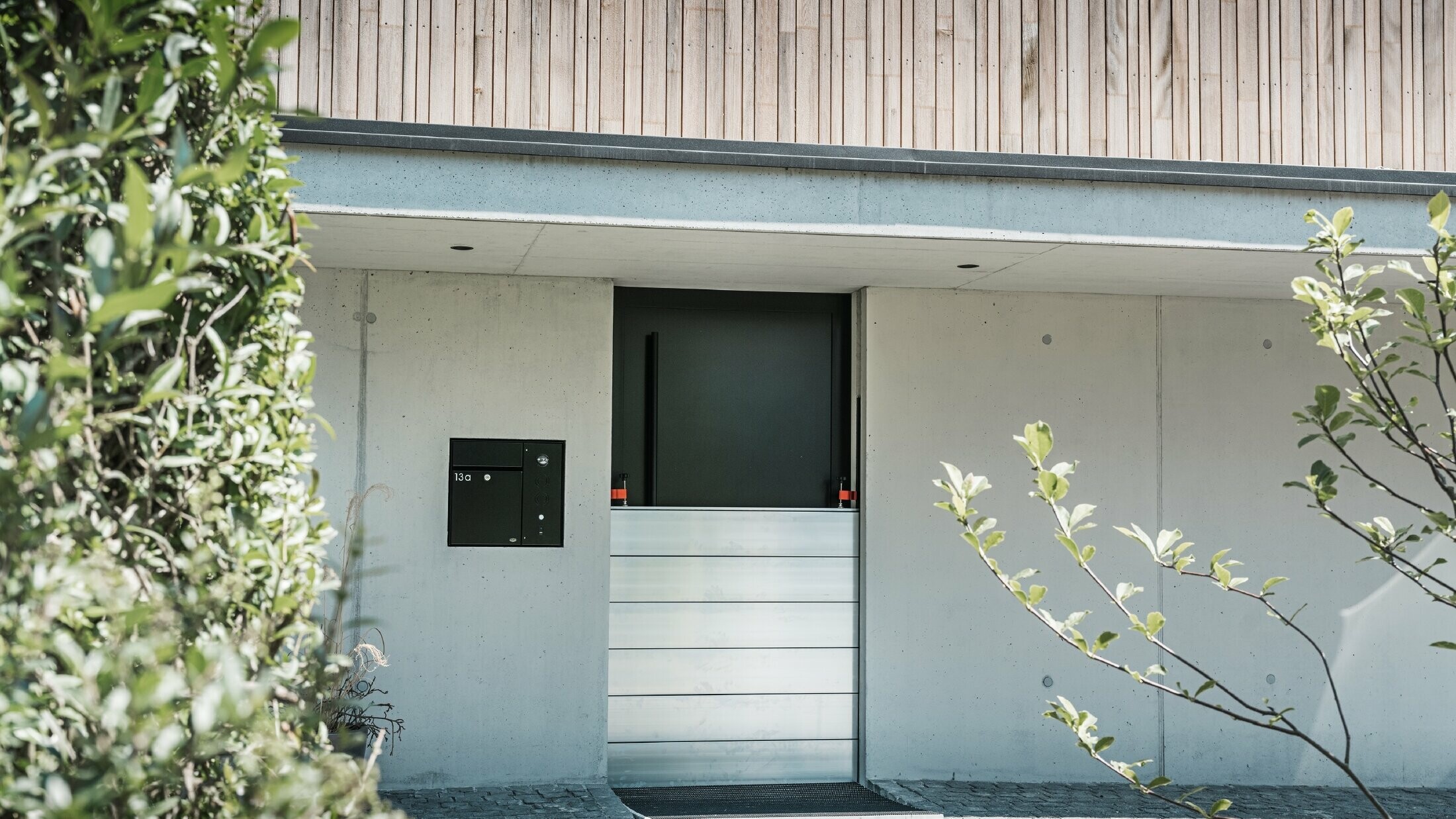 Ochrona przeciwpowodziowa PREFA została zainstalowana przed drzwiami wejściowymi domu jednorodzinnego z drewnianą fasadą. 