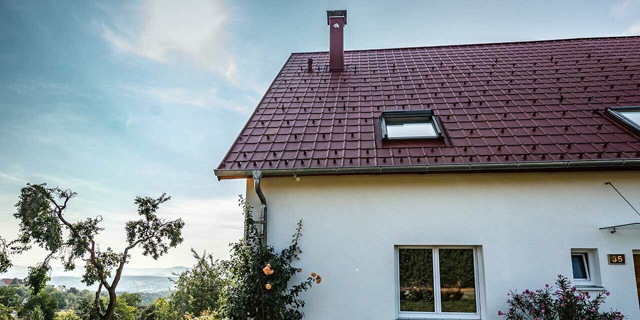 Domek na wsi z wyremontowanym dachem z dachówki klasycznej PREFA w kolorze czerwonym tlenkowym, oknami dachowymi i obróbką komina.