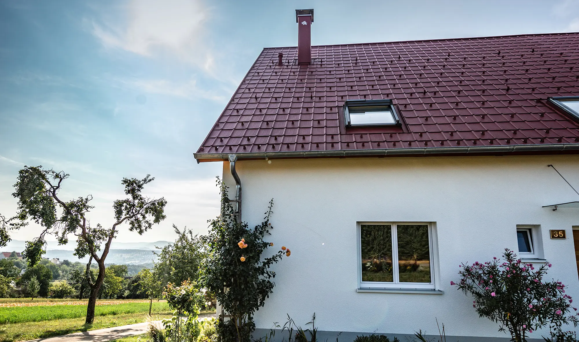 Domek na wsi z wyremontowanym dachem z dachówki klasycznej PREFA w kolorze czerwonym tlenkowym, oknami dachowymi i obróbką komina.