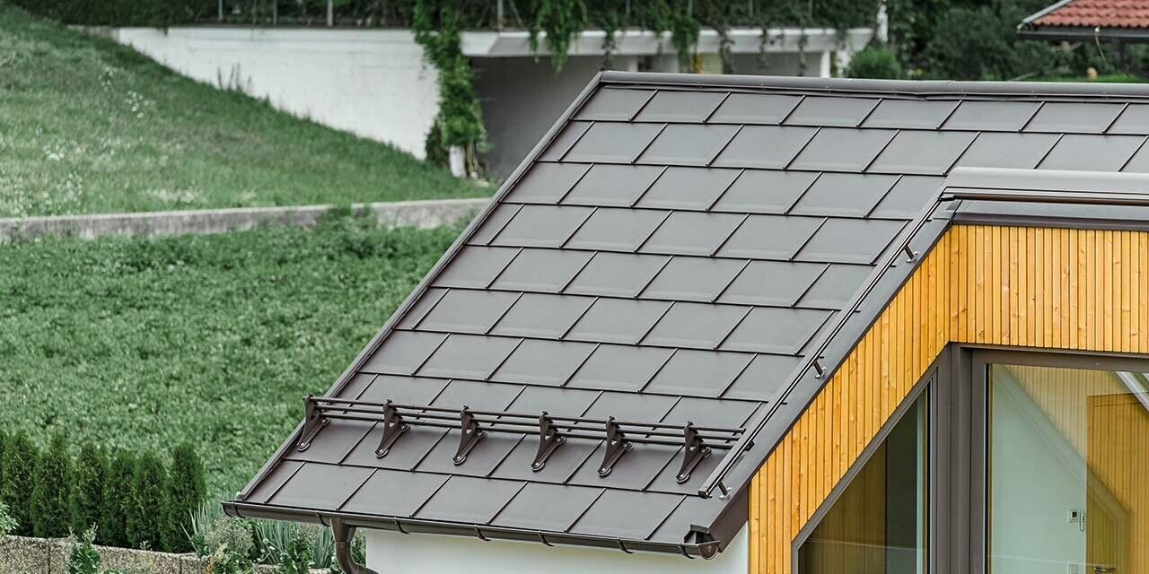 Dach dwuspadowy domu mieszkalnego przykryty dachówką klasyczną R.16 PREFA w kolorze orzechowy brąz. Wykorzystano także system bariery śniegowej PREFA;