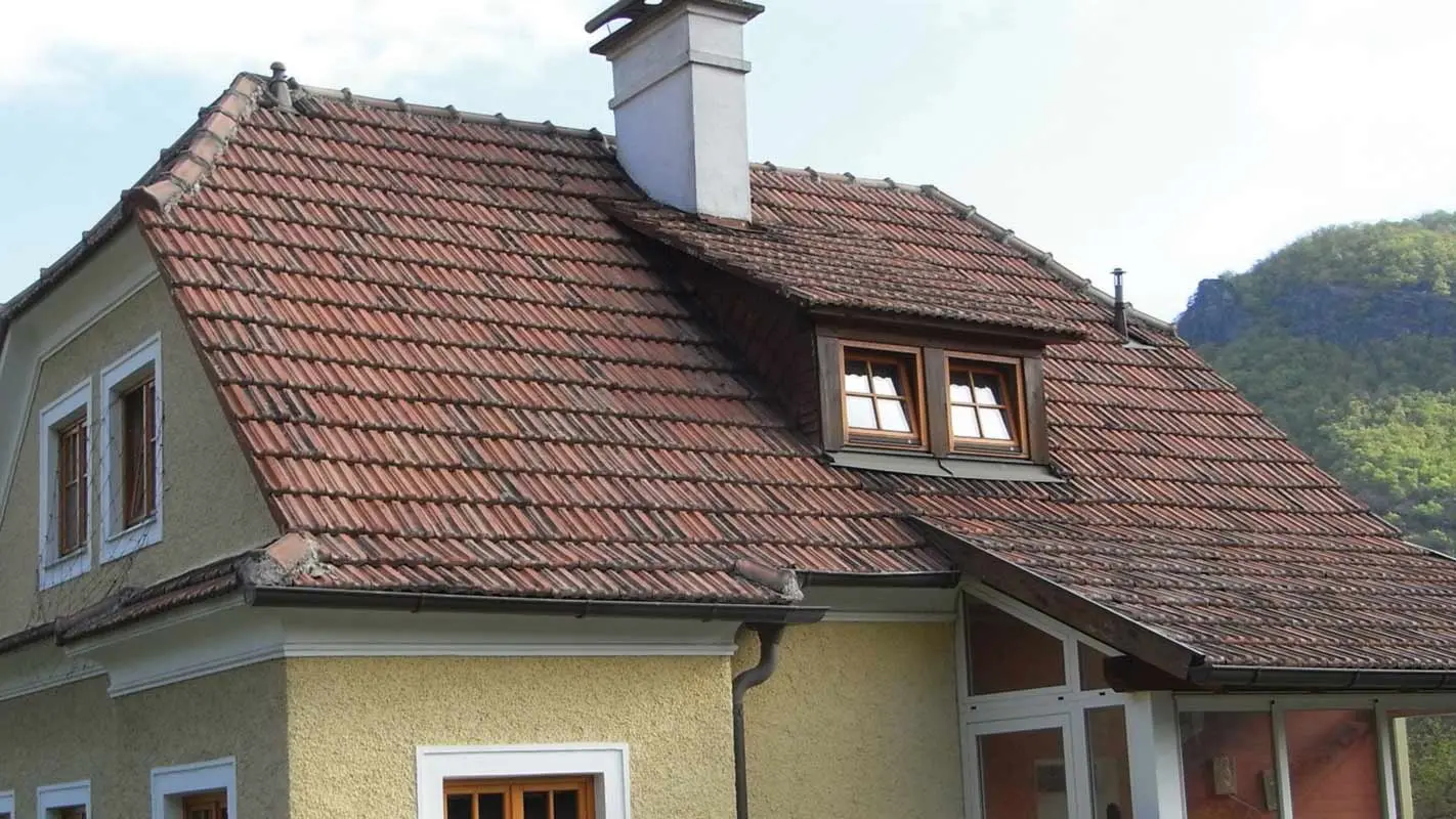 Stary dom jednorodzinny przed modernizacją dachu z dachówką i chropowatą, żółtą elewacją tynkową