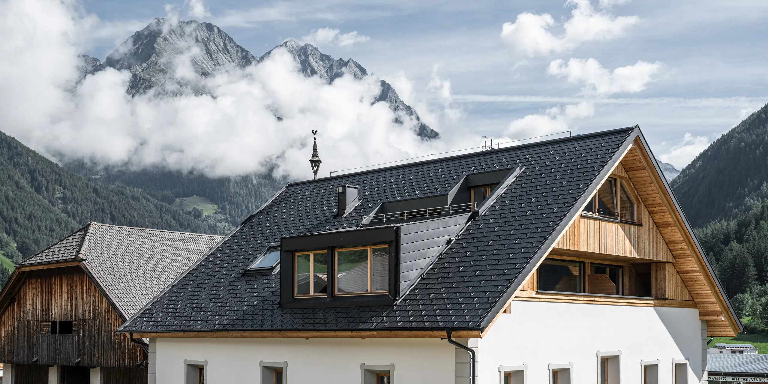Detailansicht des wind- und wetterfesten PREFA Dachsystems. Das Satteldach des Außerwegerhofs in Südtirol wurde mit robusten PREAF DS.19 Dachschindeln in P.10 anthrazit eingedeckt. Die ästhetische Dachgestaltung ist umgeben von der beeindruckenden Bergkulisse des Antholzertals.