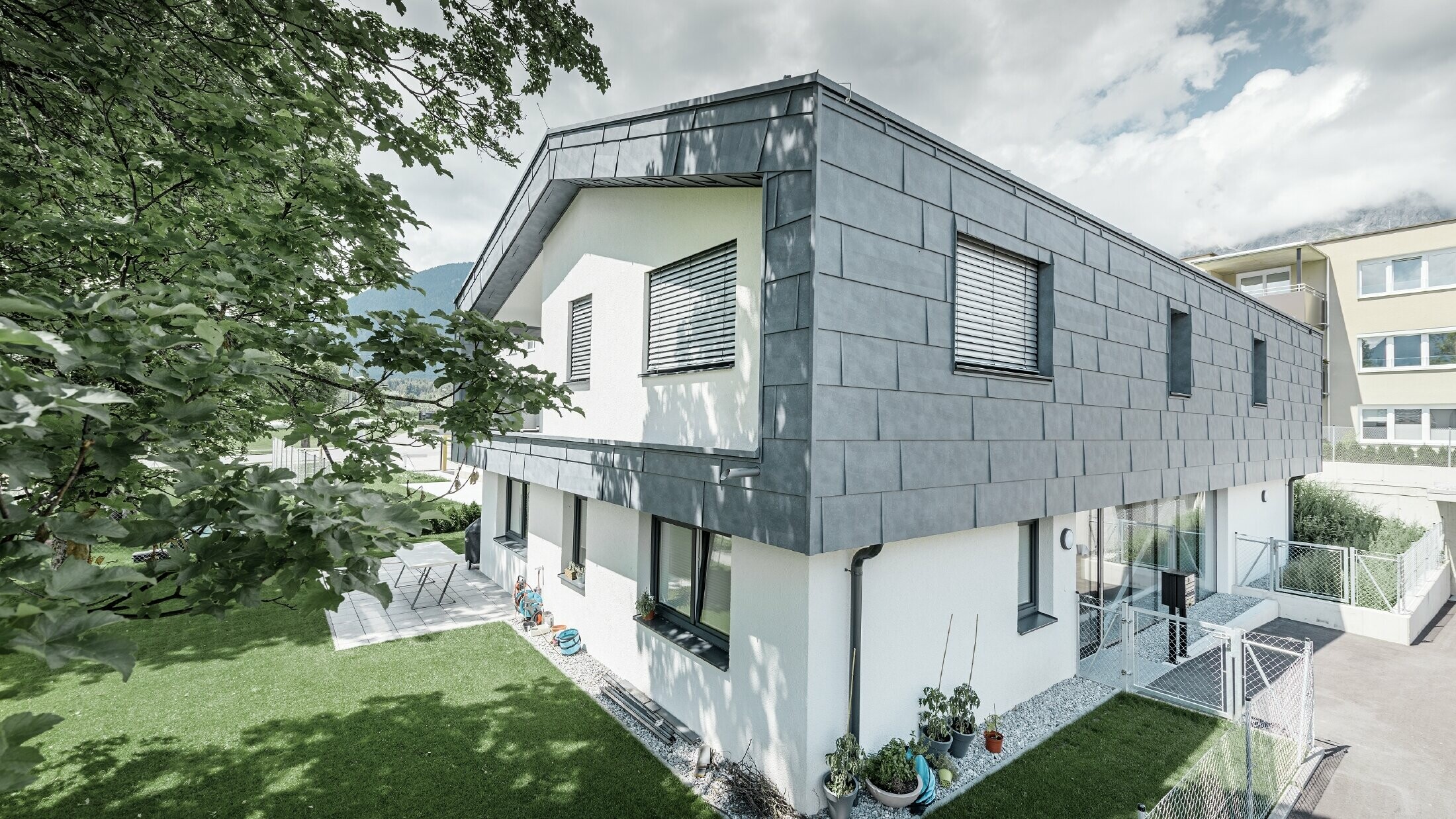 Nowoczesne podwyższenie domu mieszkalnego z płaskim dachem dwuspadowym i bez okapu. Poszycie elewacji wykonano z panelu elewacyjnego PREFA FX.12 w kolorze szarym kamiennym.