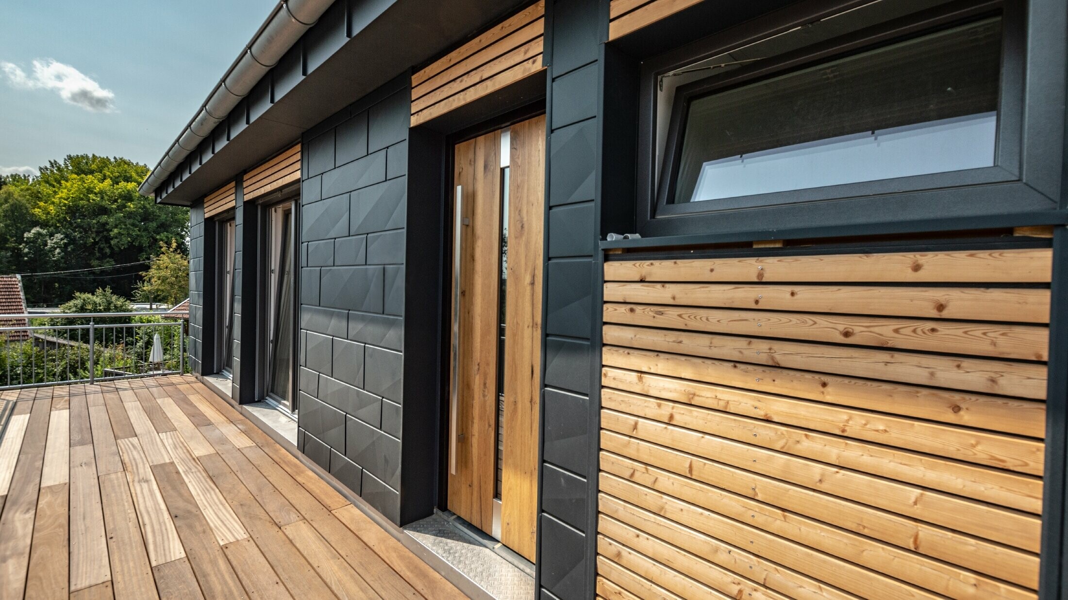 Aranżacja elewacji wykonana z aluminium w postaci PREFA Siding.X w kolorze antracytowym przekładanego drewnianymi listwami.