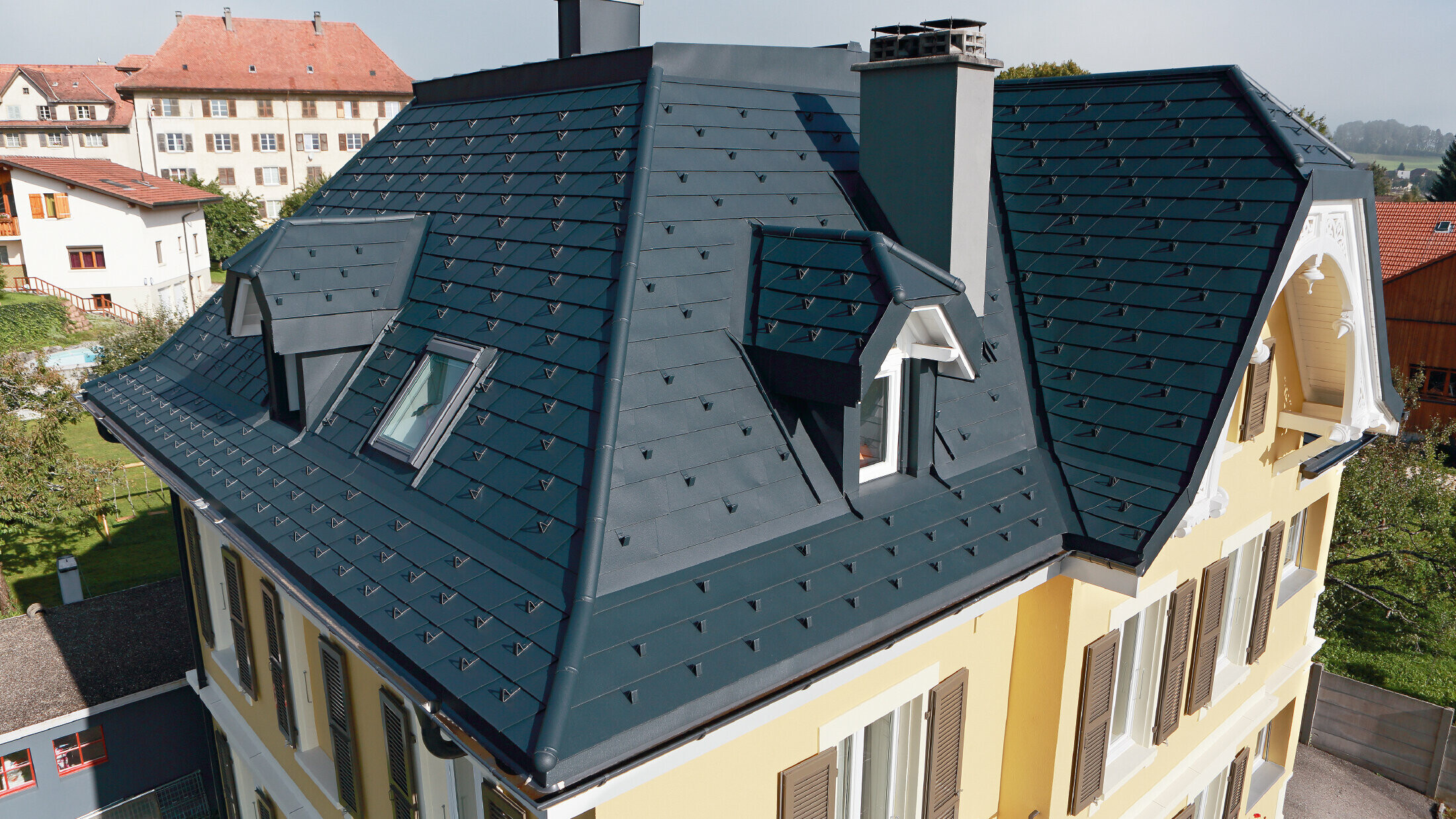 Willa w Szwajcarii, dach z licznymi koszami i małymi lukarnami, dach jest pokryty aluminiową dachówką łupkową PREFA w kolorze P.10 antracyt.